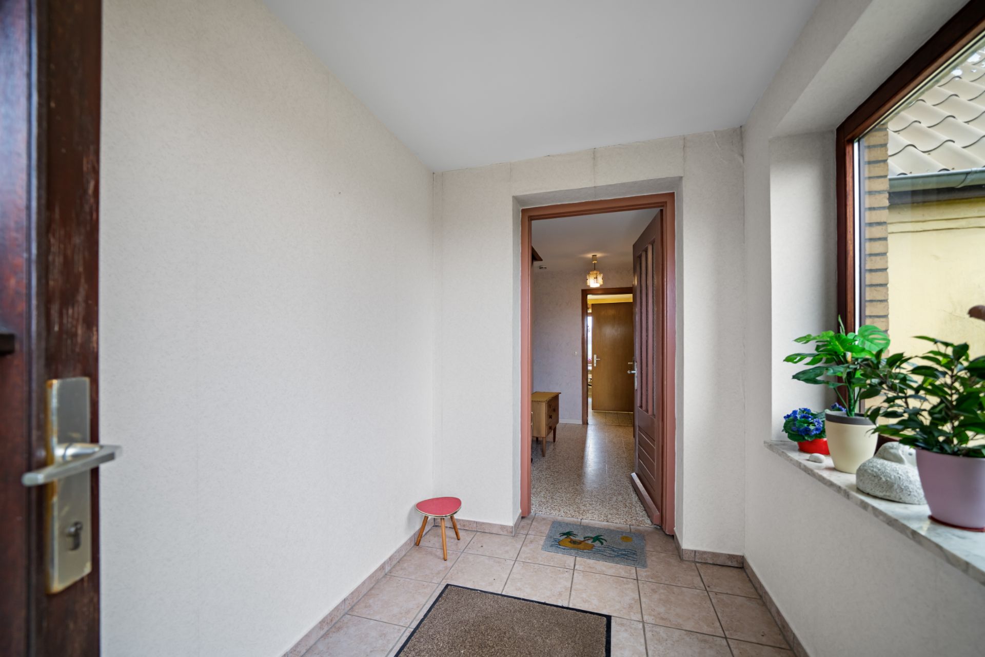 Eingangsbereich mit Fliesenboden, kleinem Hocker und Fensterbank mit Pflanzen.
