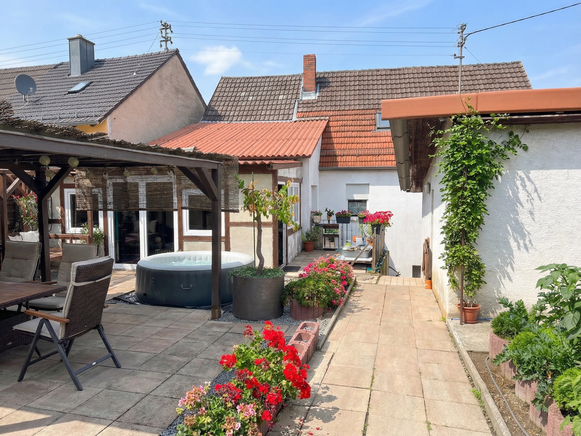 Gepflasterter Hinterhof mit Blumen, Sitzecke, Pavillon und aufblasbarem Whirlpool.