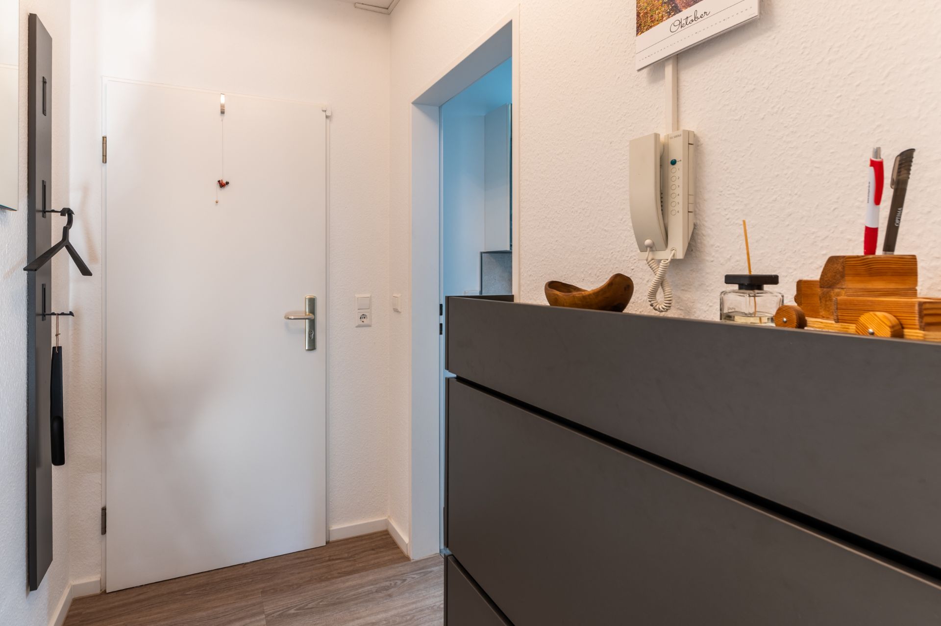 Flur mit Eingangstür, Kommode, Wandtelefon und Garderobe mit Kleiderbügel.