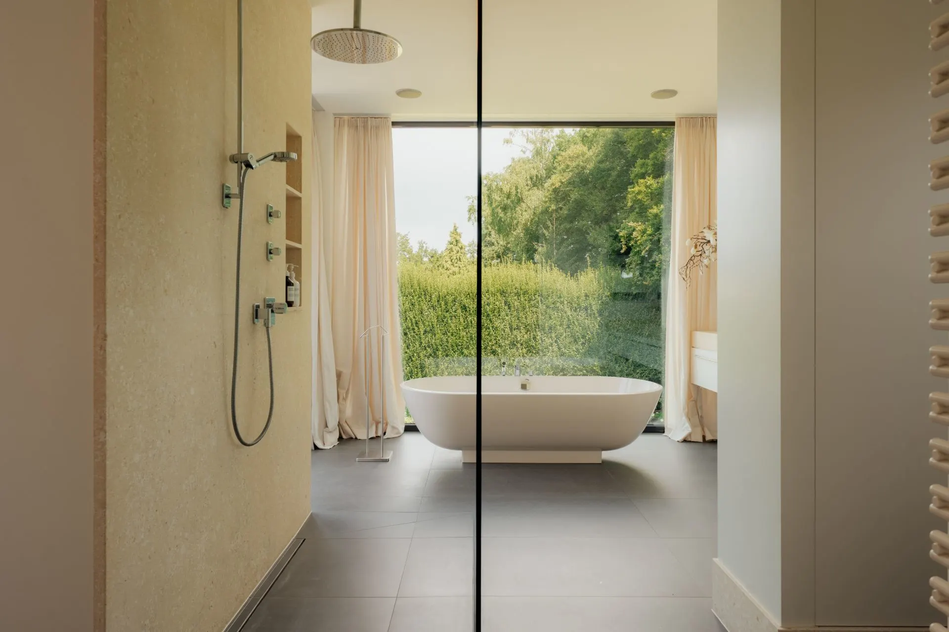 Modernes Badezimmer mit freistehender Badewanne vor großem Fenster und Dusche links.