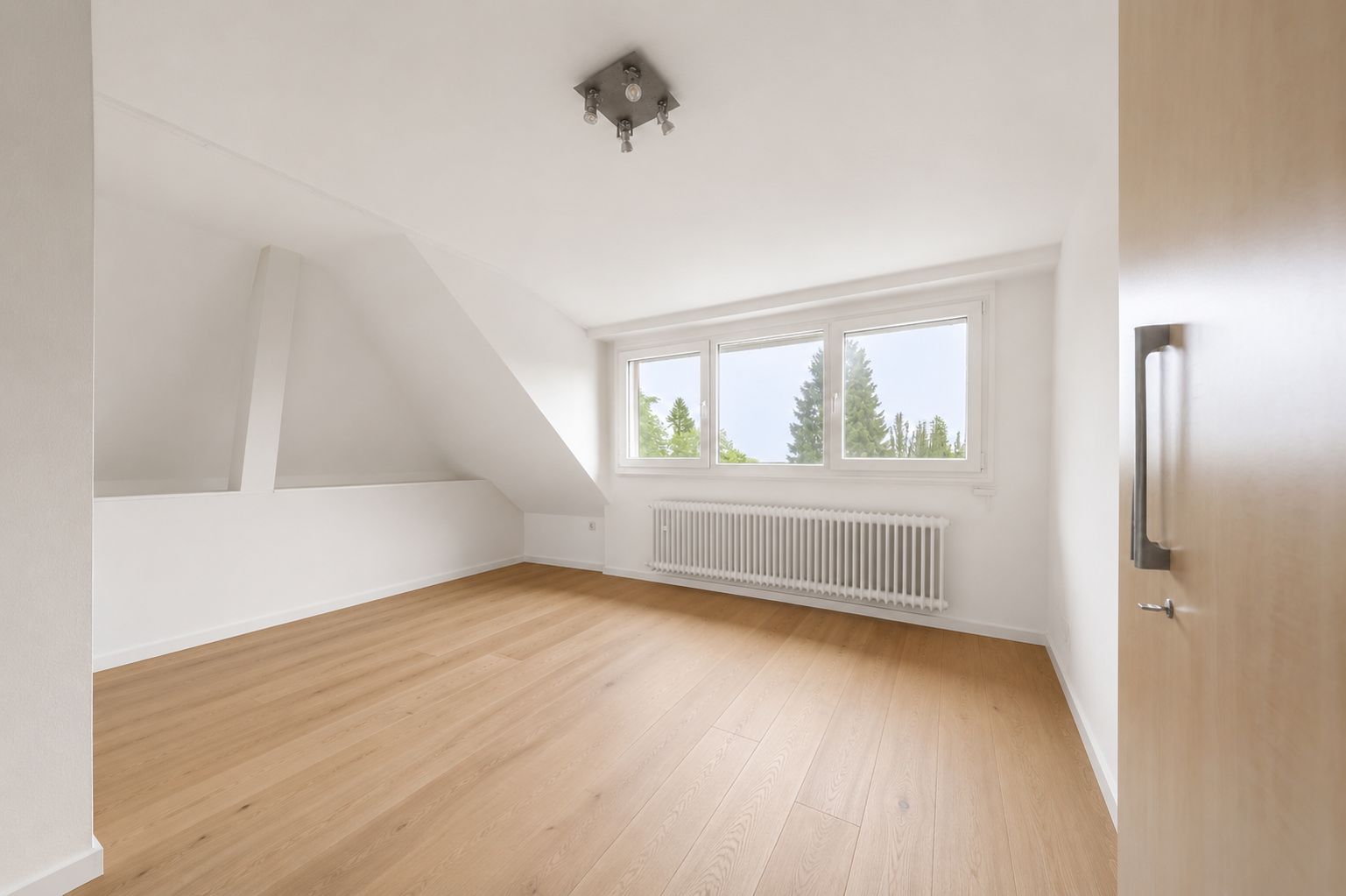 Helles, leeres Zimmer mit Holzfußboden, drei Fenstern und weißem Heizkörper.