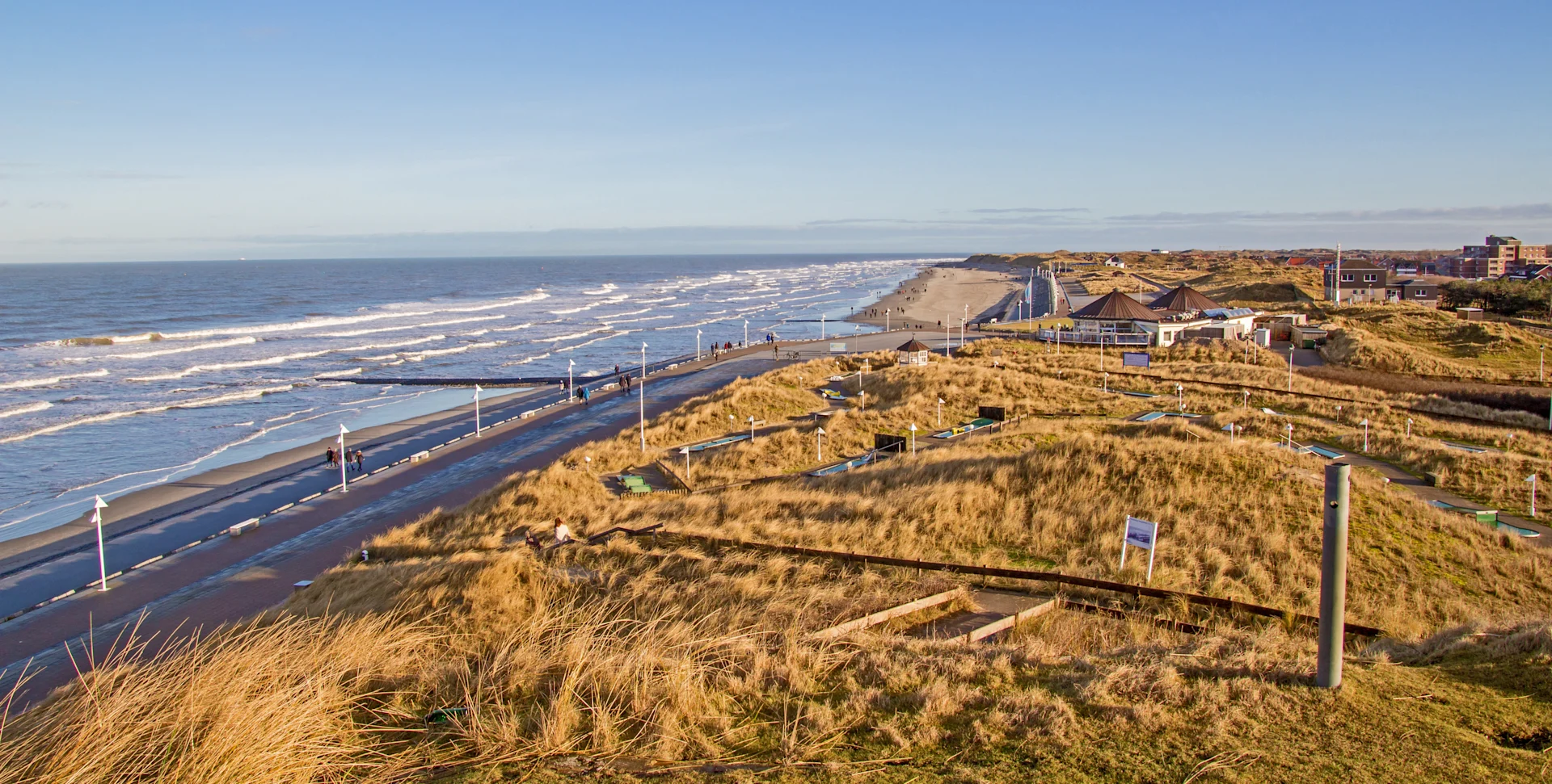 Blick auf eine Dünenlandschaft mit Weg, der entlang der Küste zum Meer verläuft.