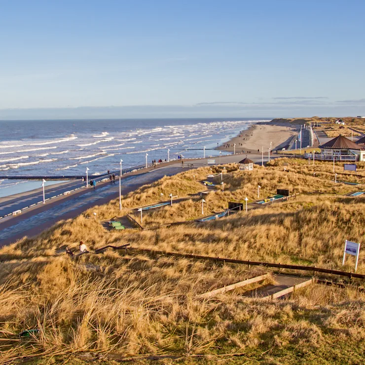 Blick auf eine Dünenlandschaft mit Weg, der entlang der Küste zum Meer verläuft.