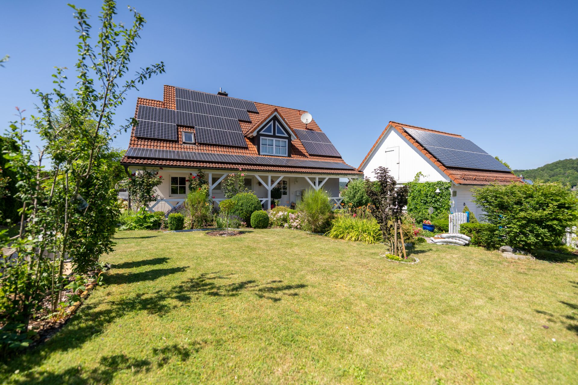 Zwei Wohnhäuser mit Solarpanels auf dem Dach, großer Garten mit Rasen und Büschen im Vordergrund.