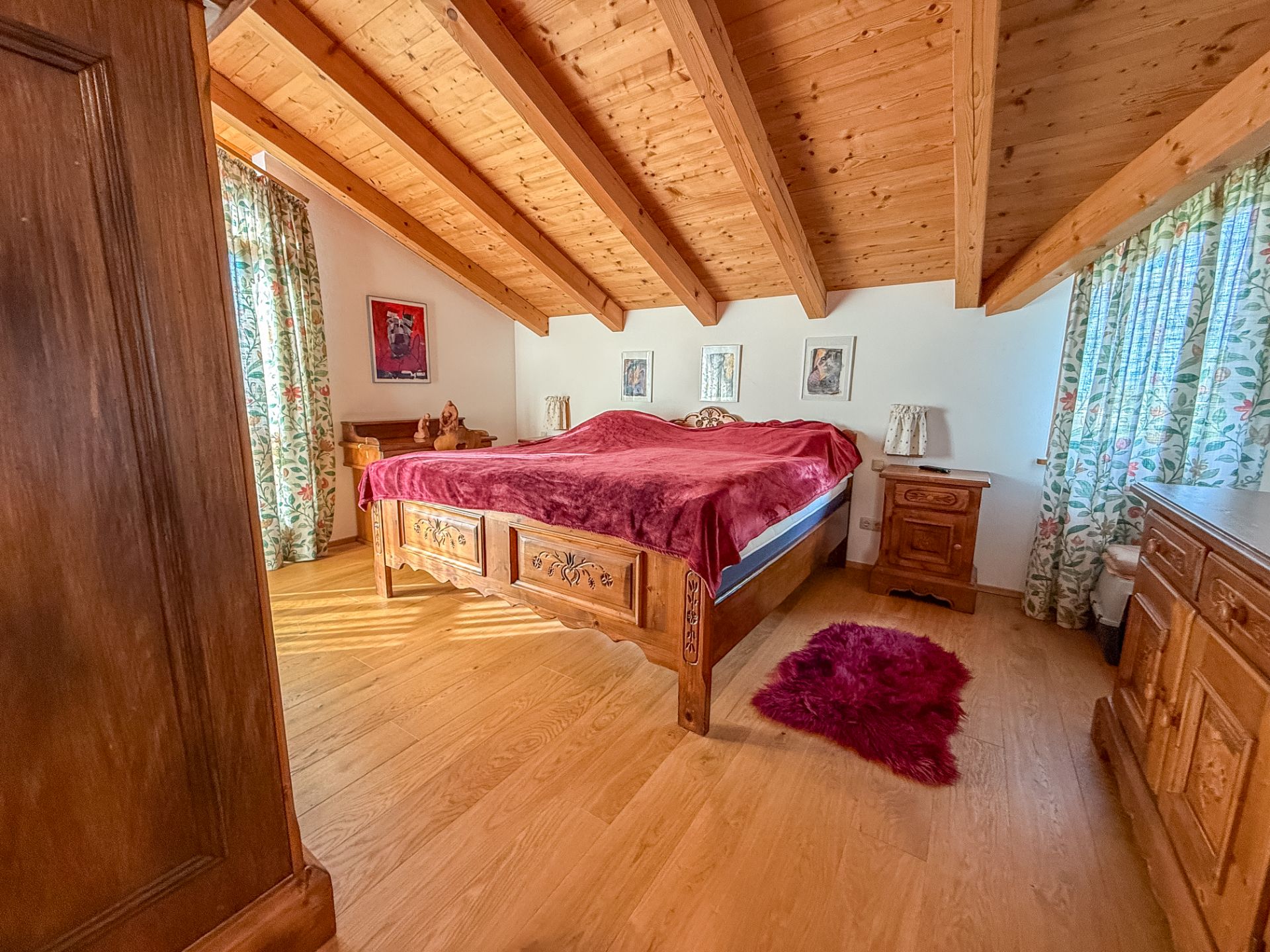 Gemütliches Schlafzimmer mit Holzboden, Holzbalkendecke und großem Bett mit roter Decke.