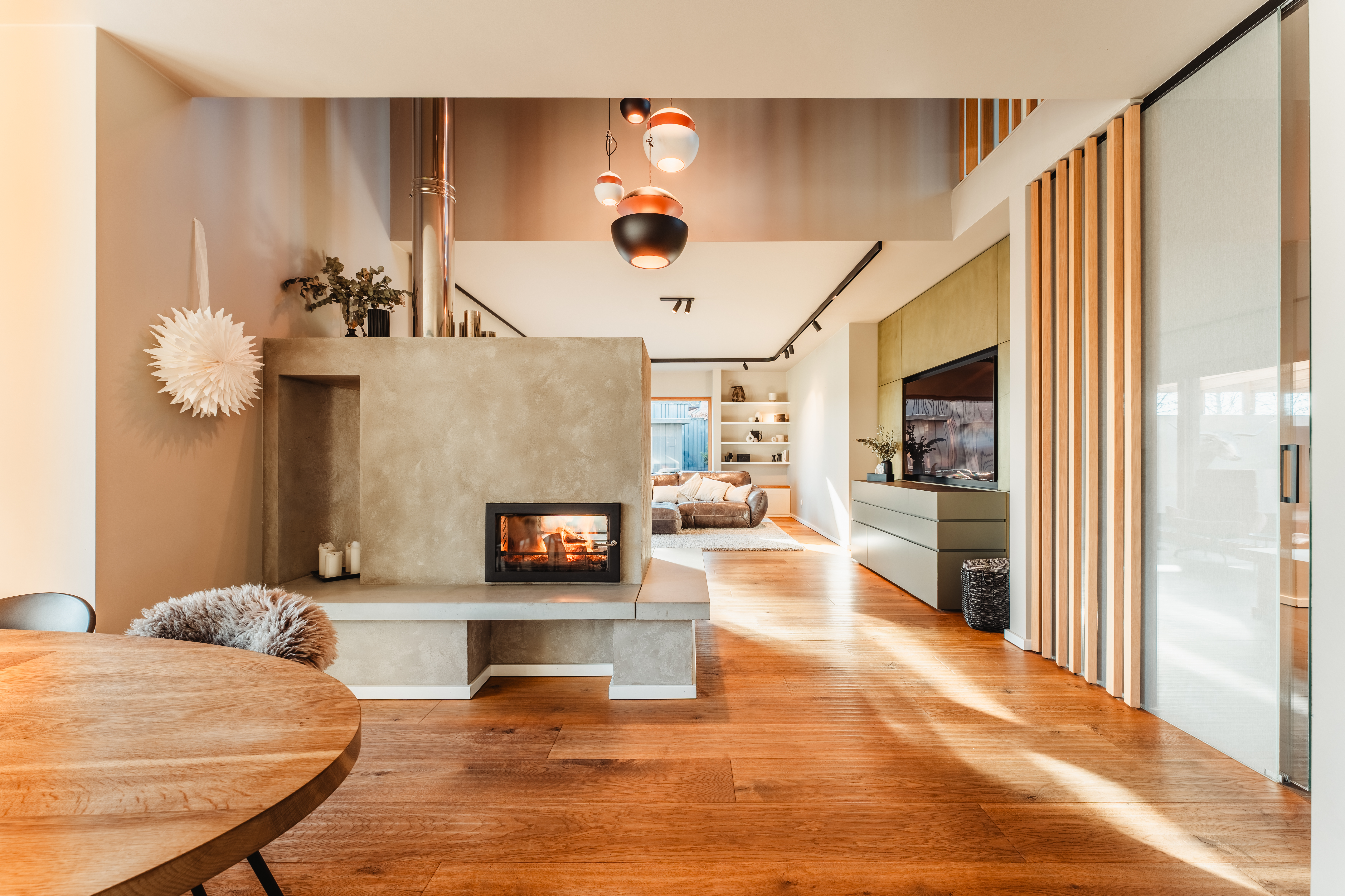 Modernes Wohnzimmer mit Kamin, Holzboden, Sofa und großen Fenstern.