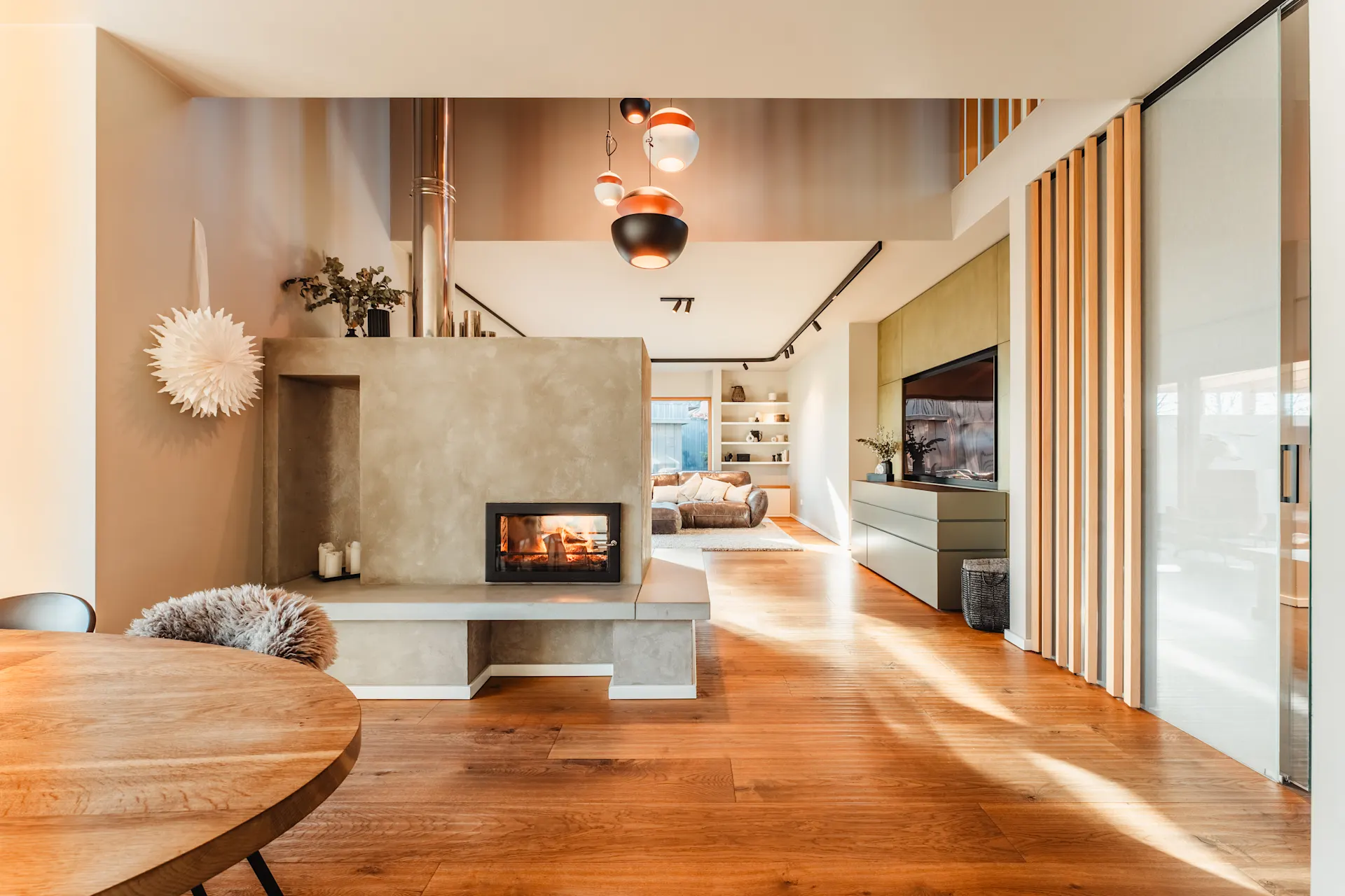Modernes Wohnzimmer mit Kamin, Holzboden, Sofa und großen Fenstern.