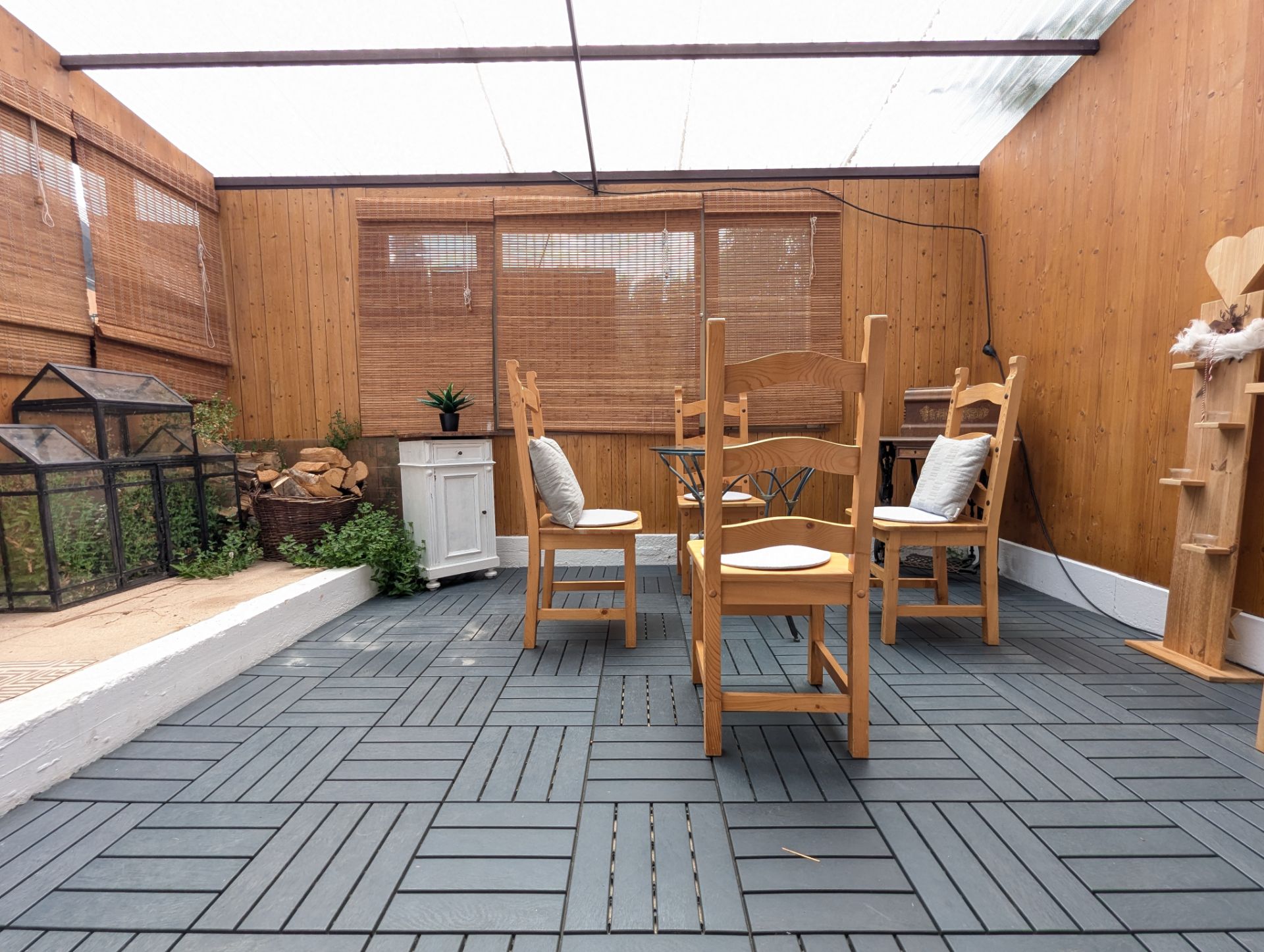 Überdachte Terrasse mit Holzwänden, vier Stühlen und Pflanzen in Töpfen.