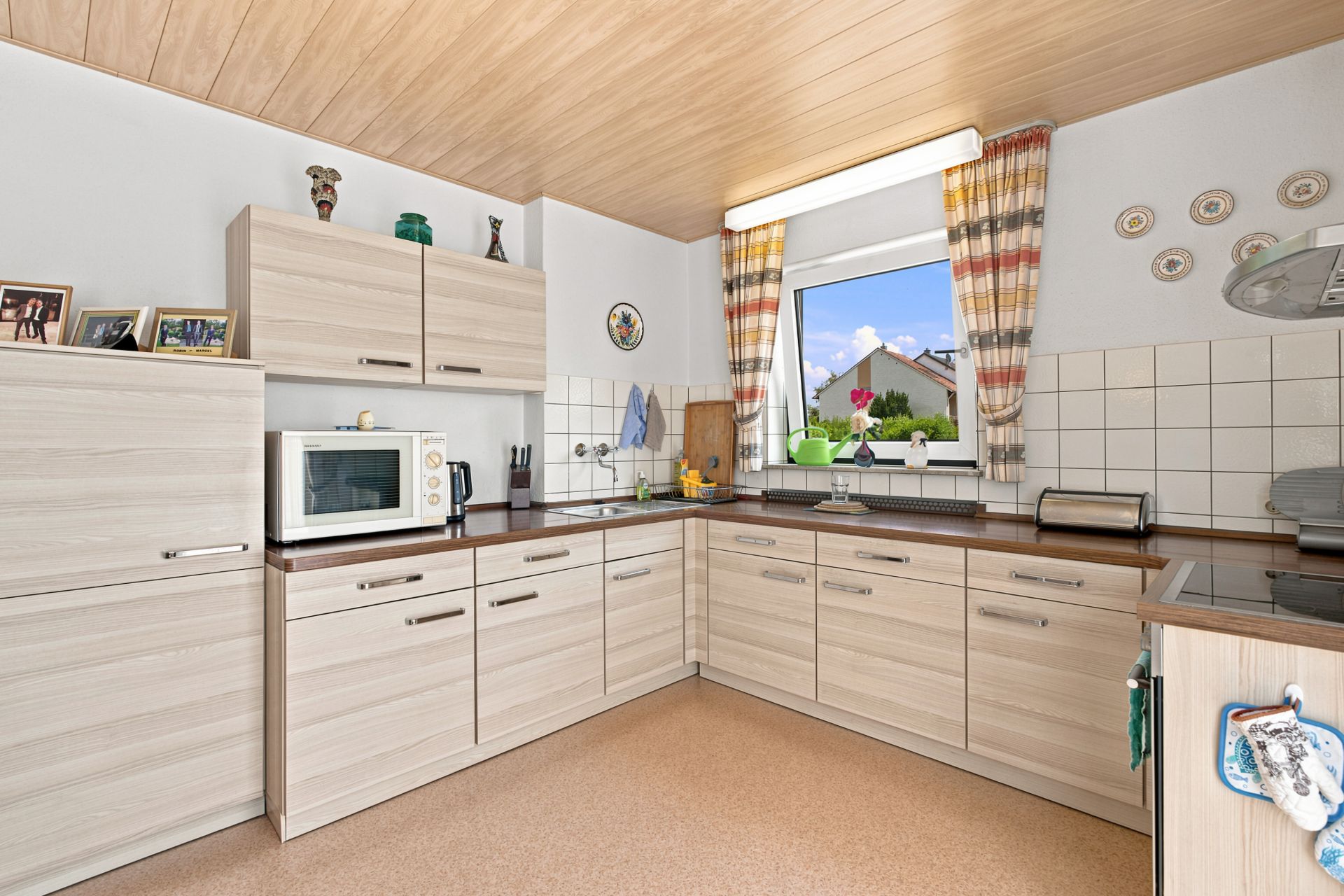 Helle Einbauküche mit Holzschränken, Fenster, Mikrowelle und Küchengeräten.