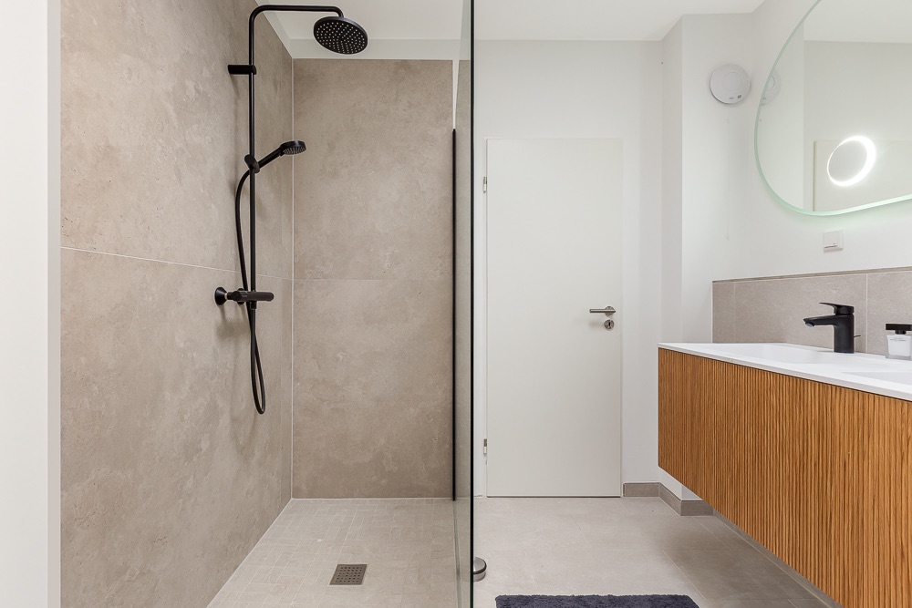 Modernes Badezimmer mit begehbarer Dusche, Holzwaschtisch und großem Spiegel.