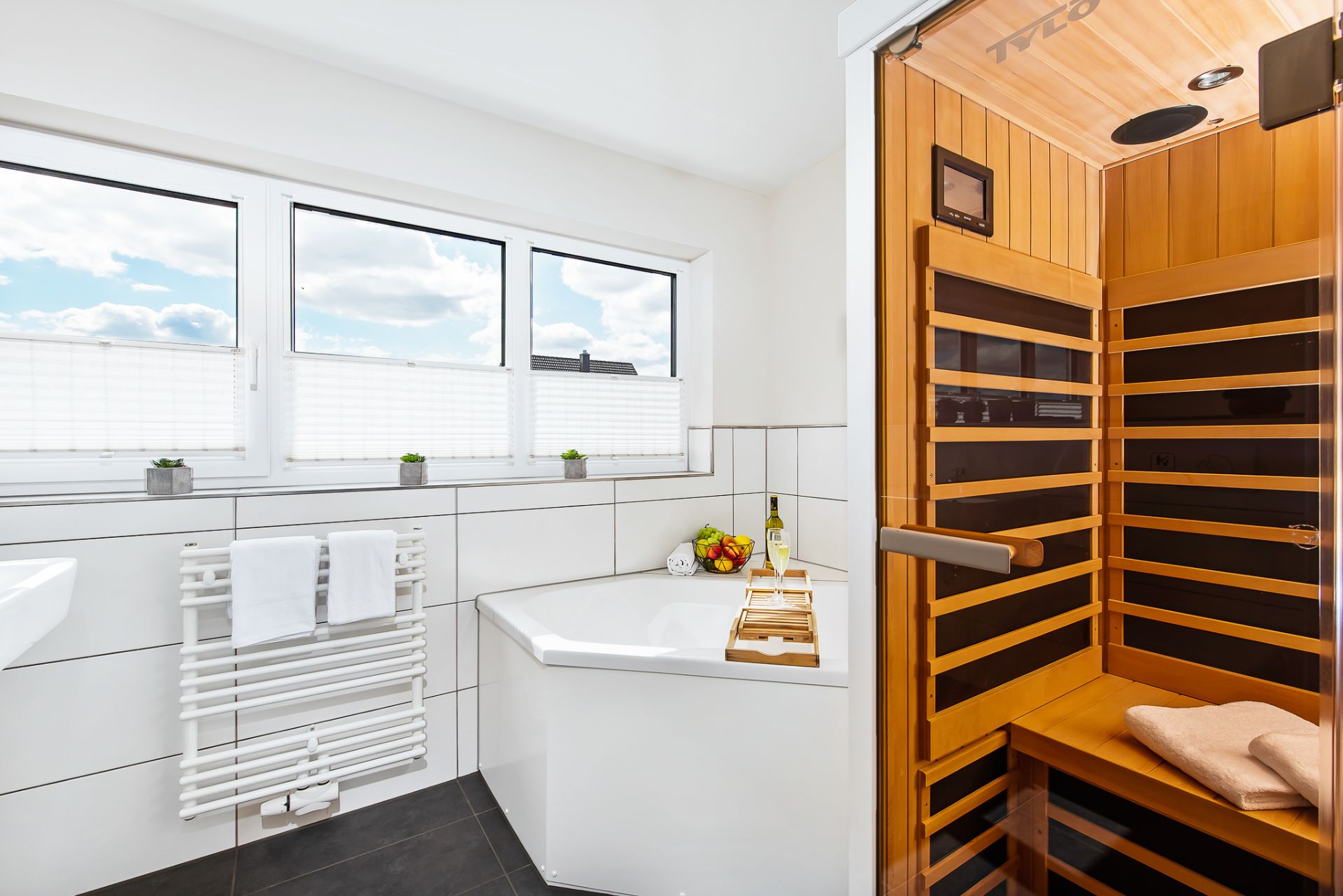 Modernes Badezimmer mit Badewanne, Sauna, Handtuchheizkörper und drei Fenstern.