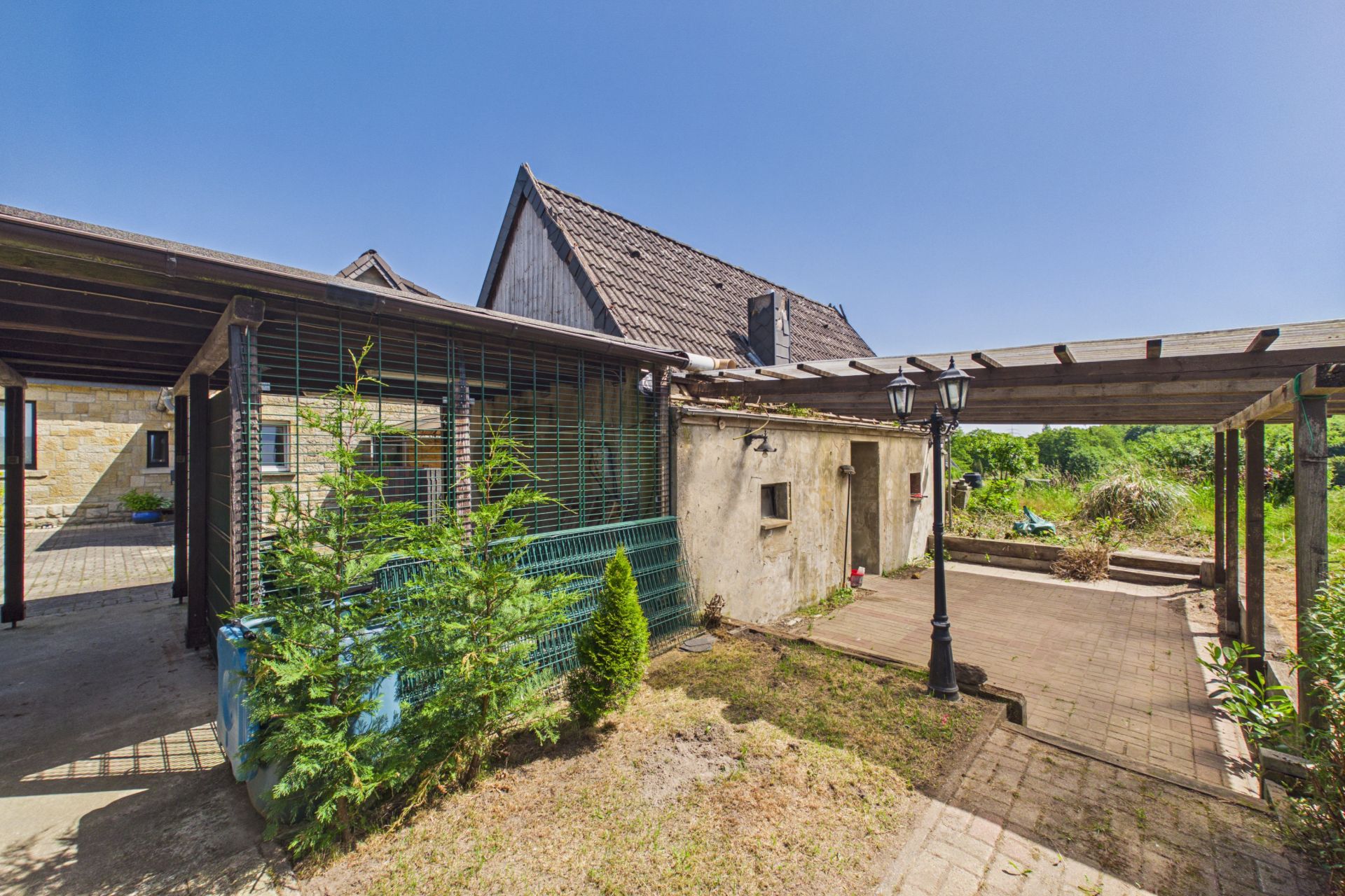 Innenhof mit überdachter Terrasse, Steinweg, kleiner Garten und Laterne, angrenzend an ein Wohnhaus.