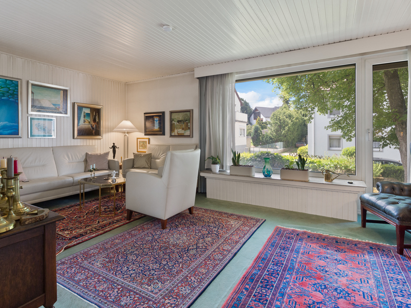 Helles Wohnzimmer mit Teppichen, weißen Sofas, großen Fenstern und mehreren Gemälden an der Wand.