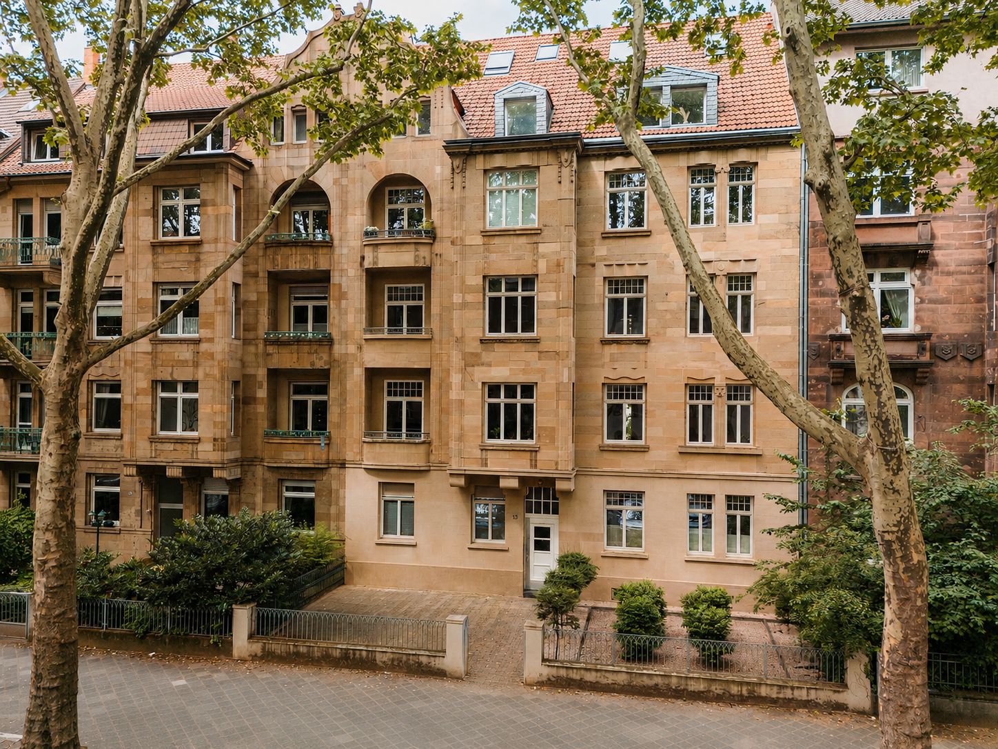 Mehrstöckiges Wohngebäude aus Sandstein mit Balkonen und Bäumen davor.