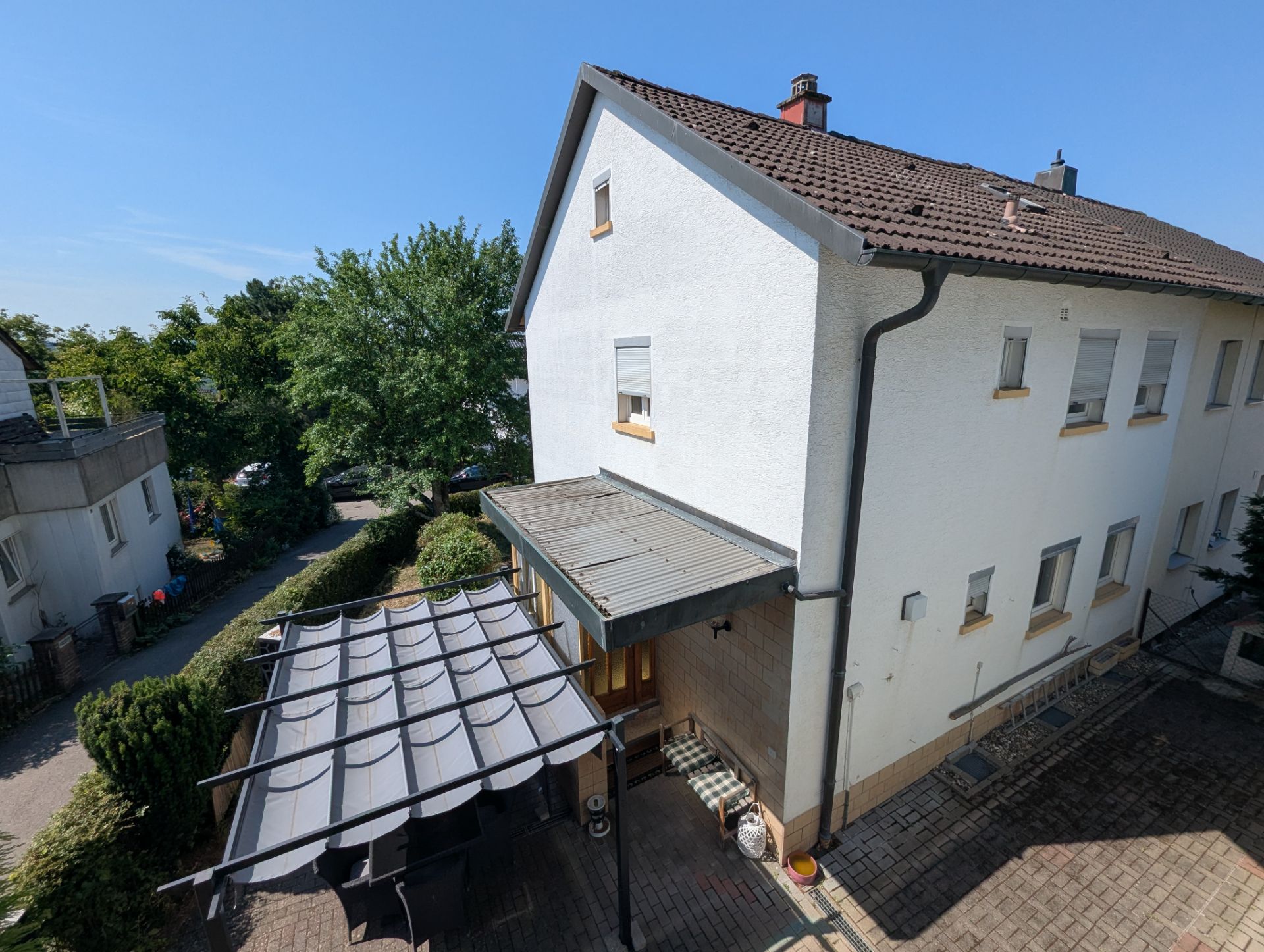 Zweistöckiges Wohnhaus mit Terrasse, Pavillon und angrenzendem Gartenbereich bei sonnigem Wetter.