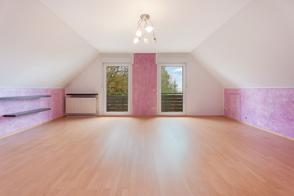 Leeres Zimmer mit schrägen Wänden, zwei Fenstern, Holzfußboden und lila Wanddeko.