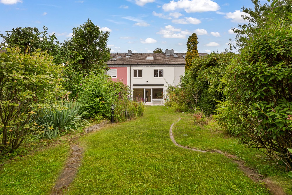 Blick auf ein Haus mit großem Garten und Rasen, umgeben von Sträuchern und Bäumen.