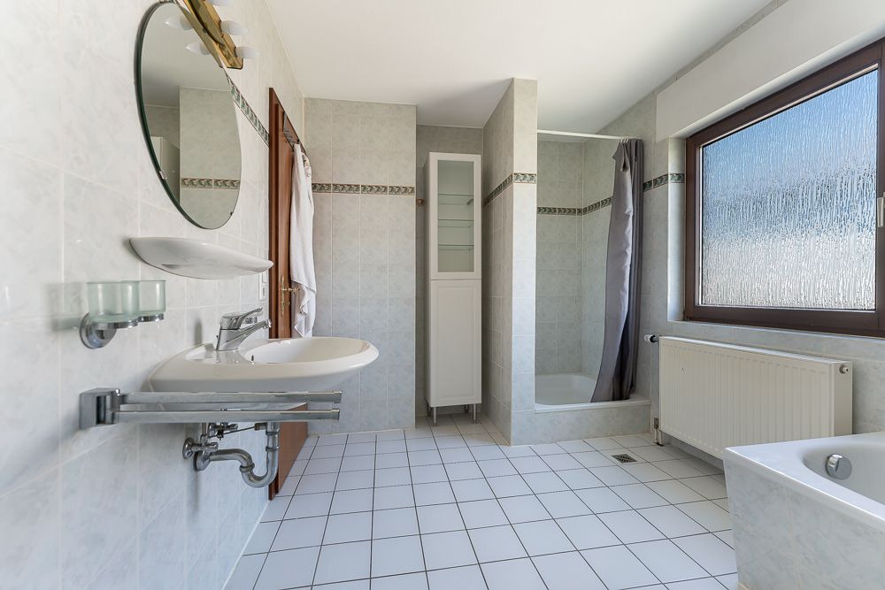 Helles Badezimmer mit Dusche, Badewanne, Waschbecken und großem Fenster.
