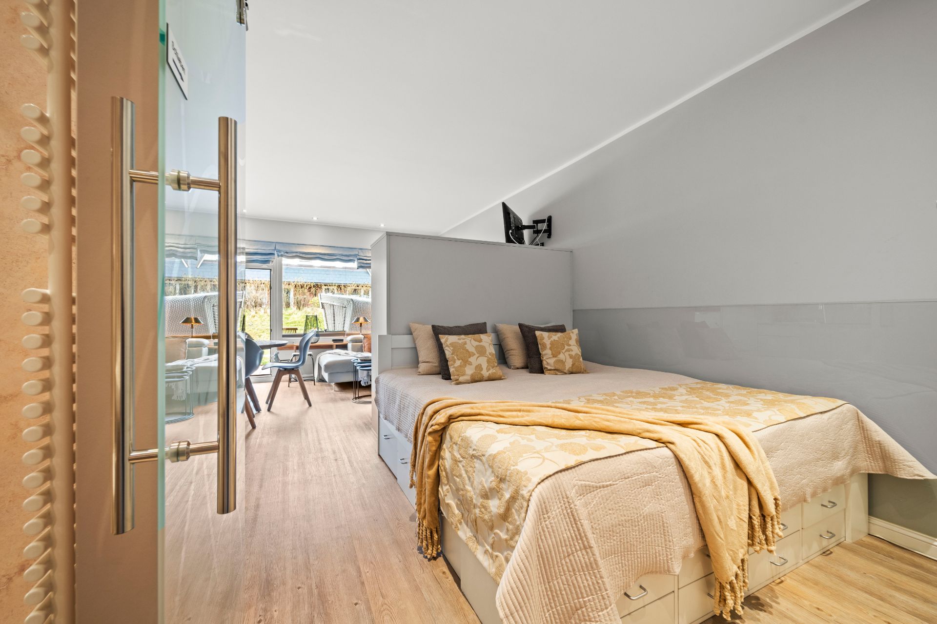 Schlafzimmer mit Doppelbett, drei Kissen, Decke und Blick auf Terrasse mit Gartenmöbeln.