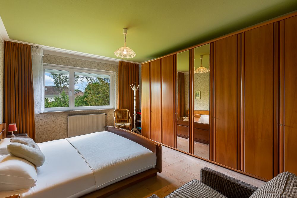 Schlafzimmer mit Doppelbett, großem Holzkleiderschrank, Fenster und Stuhl.