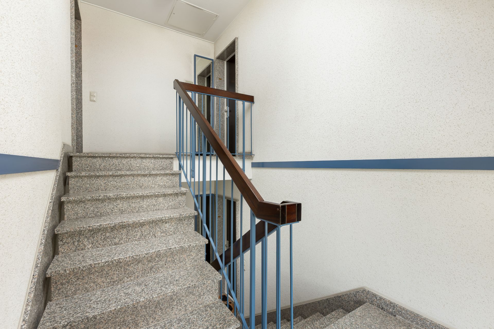 Innenansicht eines Treppenhauses mit grauen Stufen und blauem Handlauf.