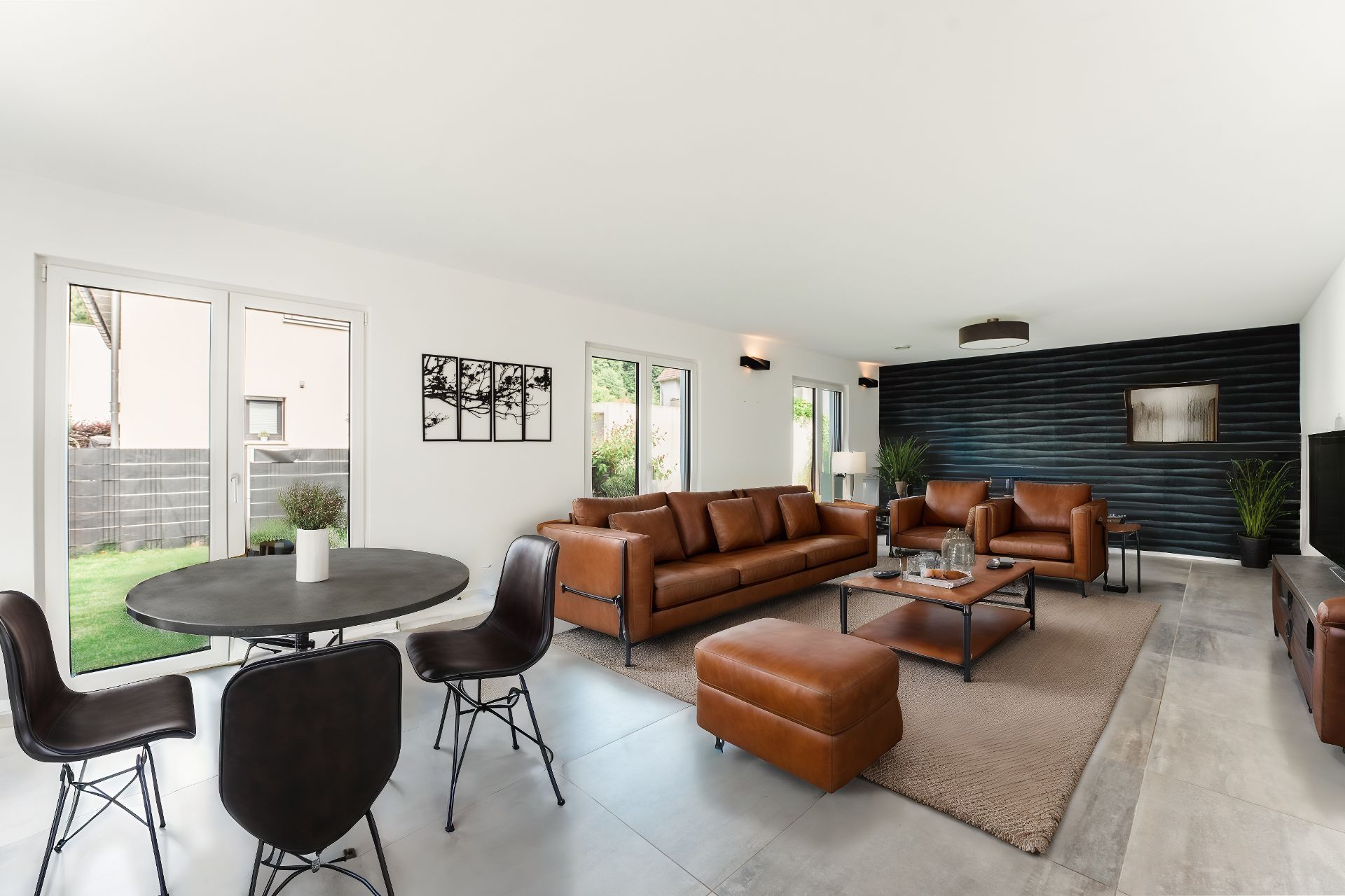 Modernes Wohnzimmer mit braunen Ledermöbeln, schwarzer Wand, Esstisch und großen Fenstern zum Garten.