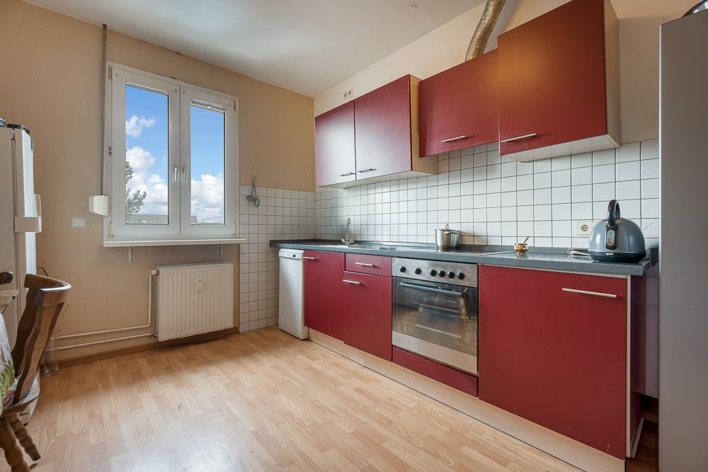 Küche mit roten Schränken, Elektroherd, Spülmaschine und Fenster mit Blick nach draußen.