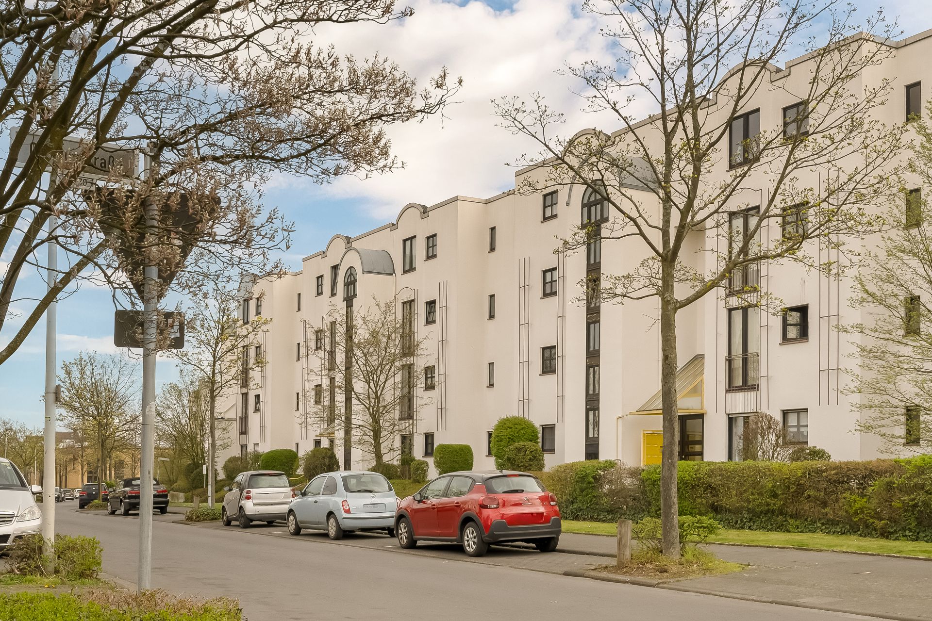 Mehrstöckiges Wohngebäude mit weißen Fassaden und geparkten Autos an einer ruhigen Straße.