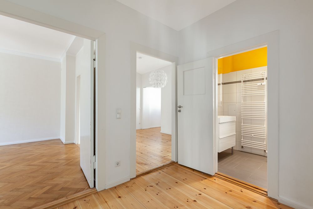 Helle Diele mit Blick in ein Wohnzimmer mit Parkett und ein Badezimmer mit gelben Akzenten.
