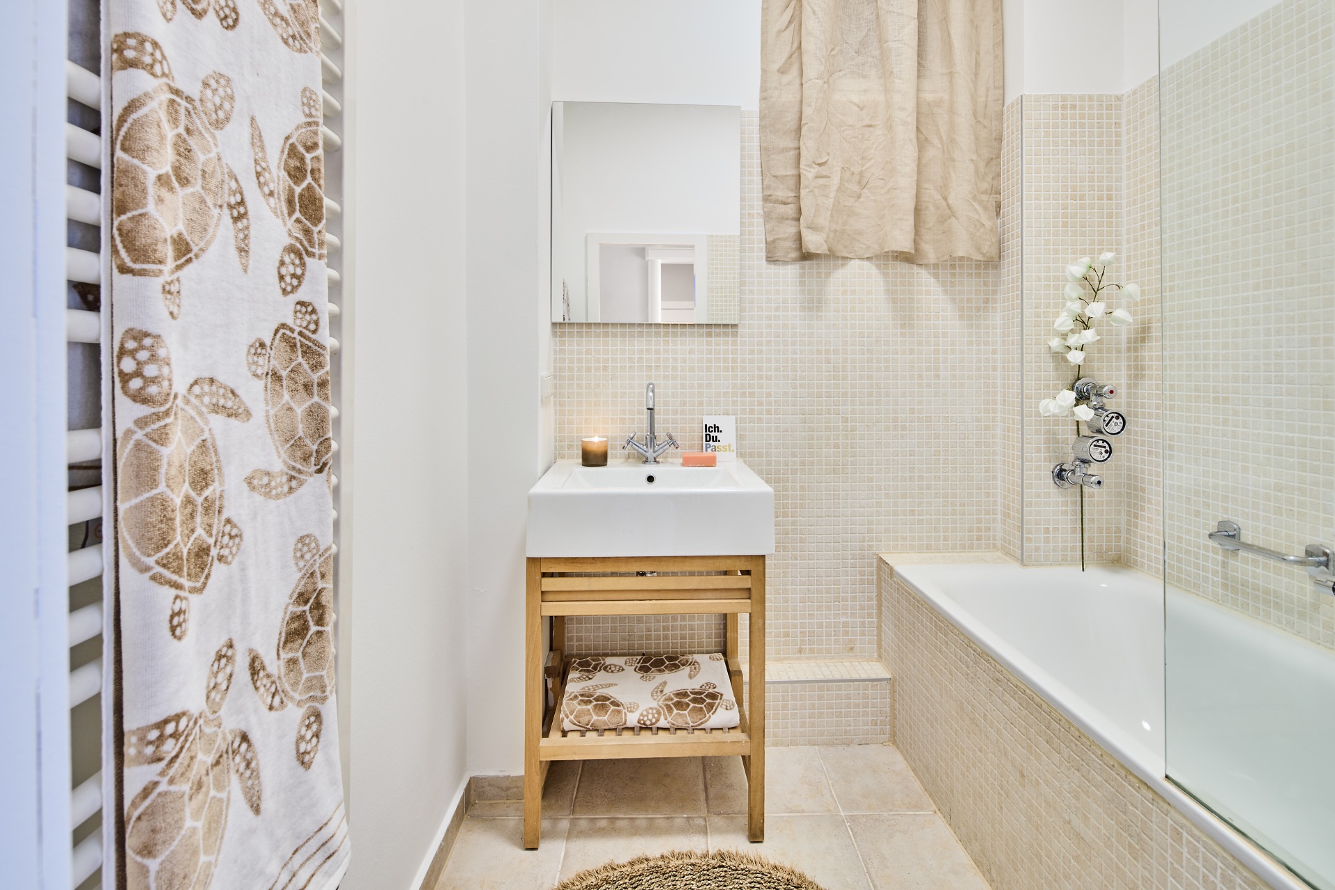 Helles Badezimmer mit Waschbecken, Badewanne, Spiegel und Handtuch mit Schildkrötenmuster.