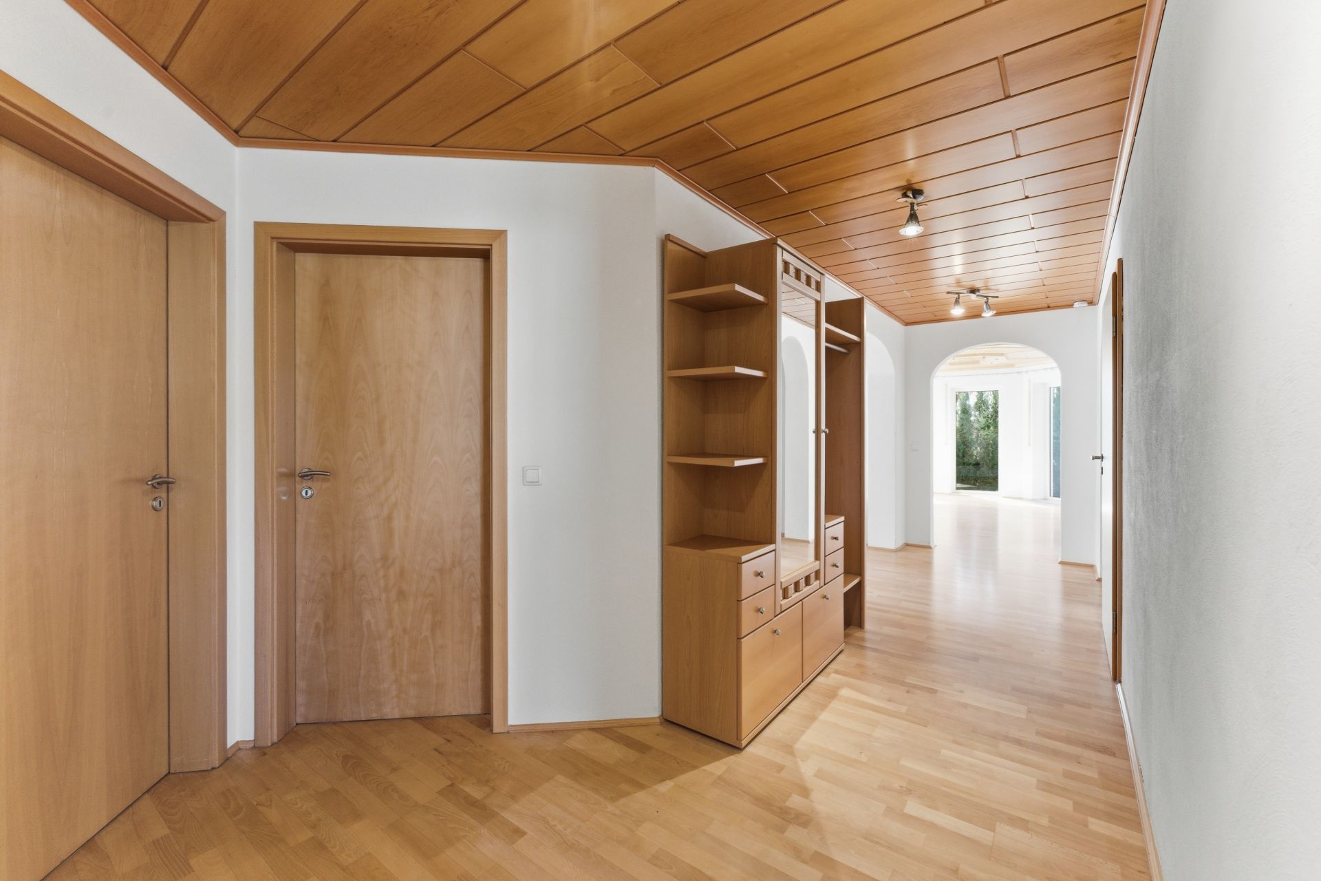 Heller Flur mit Holzdecke, Holzfußboden, drei Türen und einem großen Holzschrank mit Spiegel.