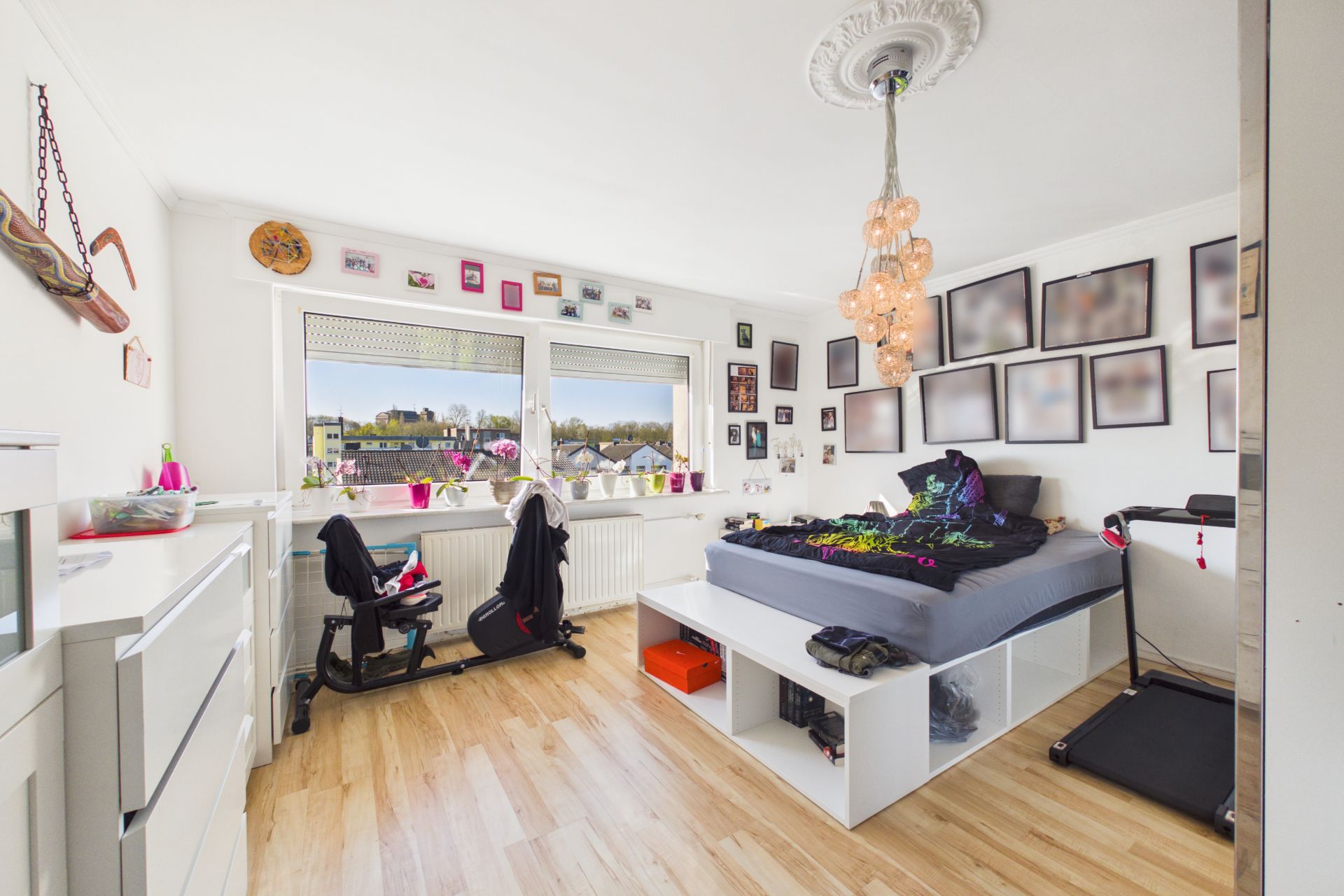 Helles Schlafzimmer mit großem Bett, vielen Bildern an der Wand und zwei Fenstern mit Ausblick.