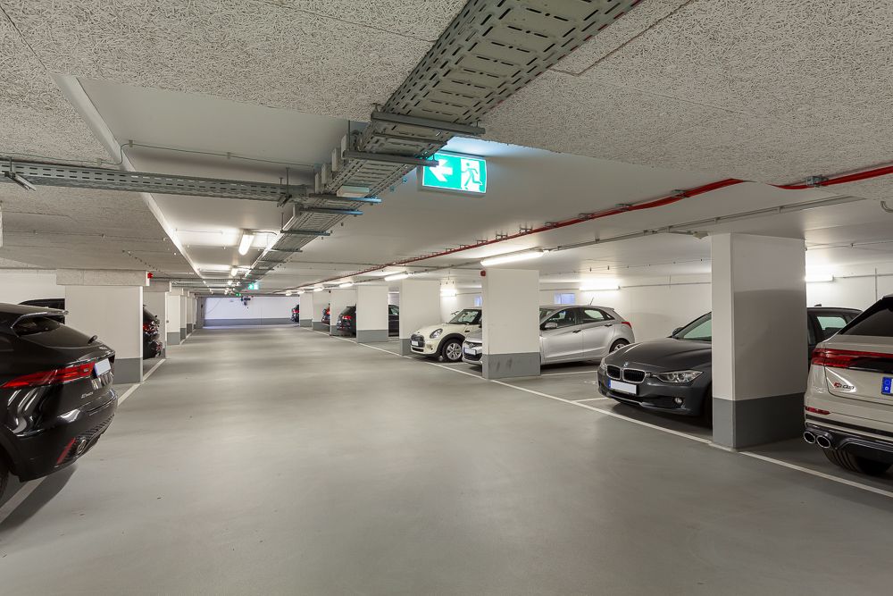 Helle Tiefgarage mit geparkten Autos und markierten Stellplätzen.