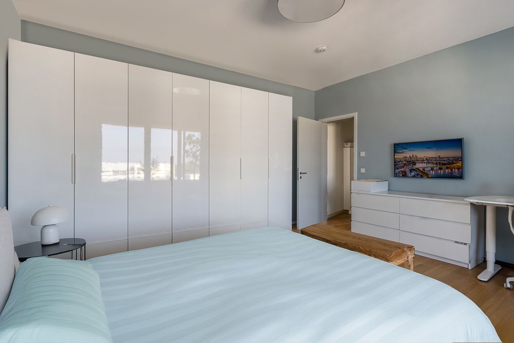 Modernes Schlafzimmer mit großem weißen Kleiderschrank, Kommode, Bett und Nachttischlampe.