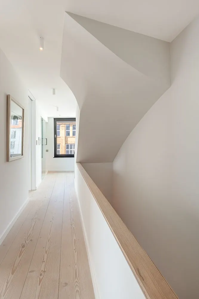 Heller Flur mit Holzfußboden, weißer Wand und modernem Fenster am Ende.