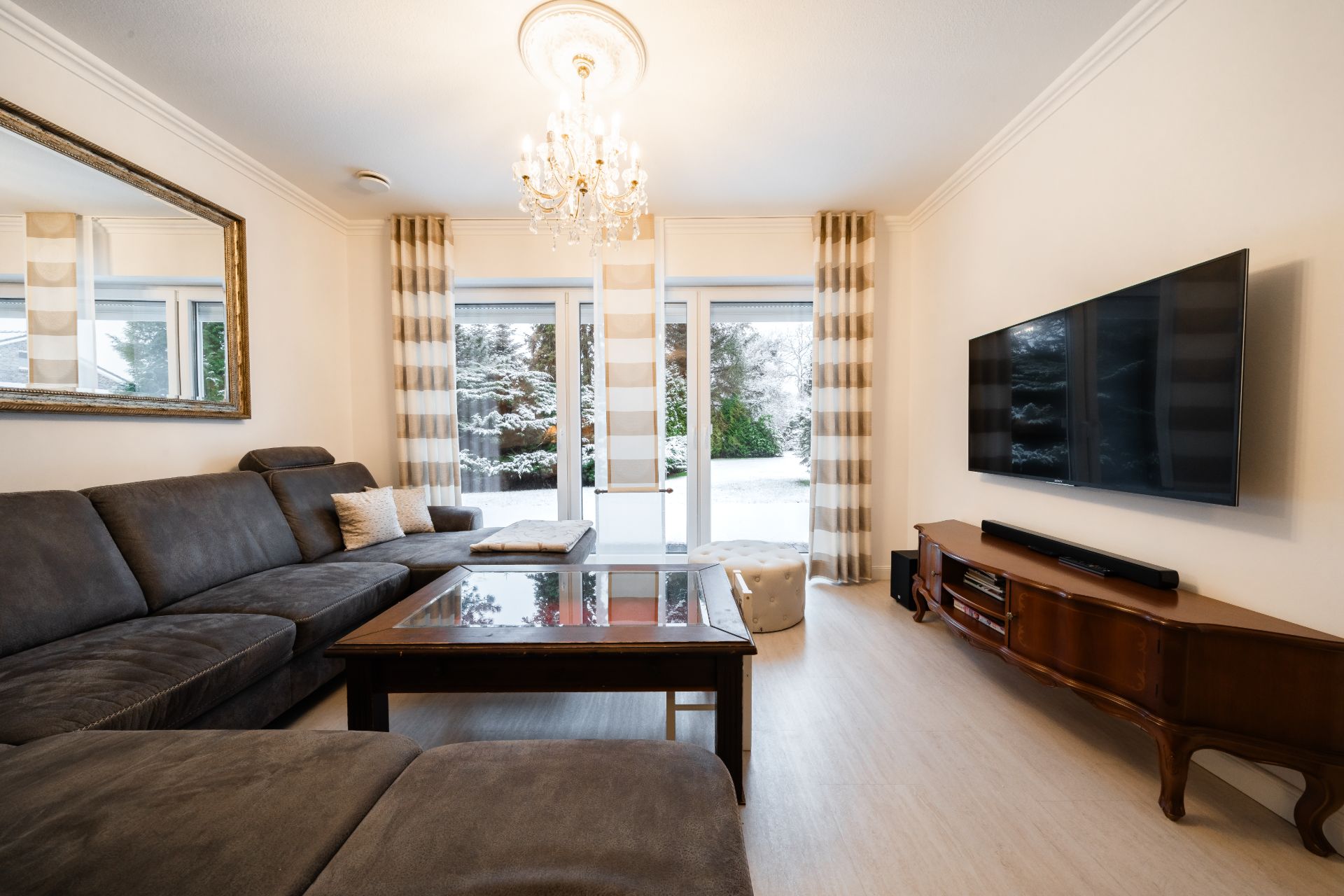 Modernes Wohnzimmer mit grauem Sofa, Glastisch, großem Fernseher und Blick auf verschneiten Garten.