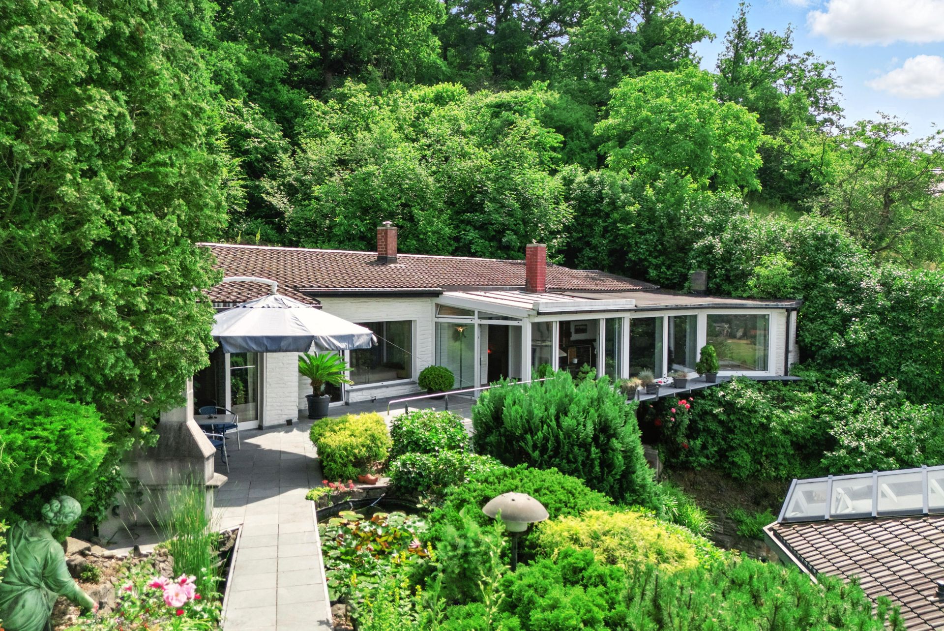 Einfamilienhaus mit großer Terrasse und gepflegtem Garten, umgeben von viel Grün und Bäumen.