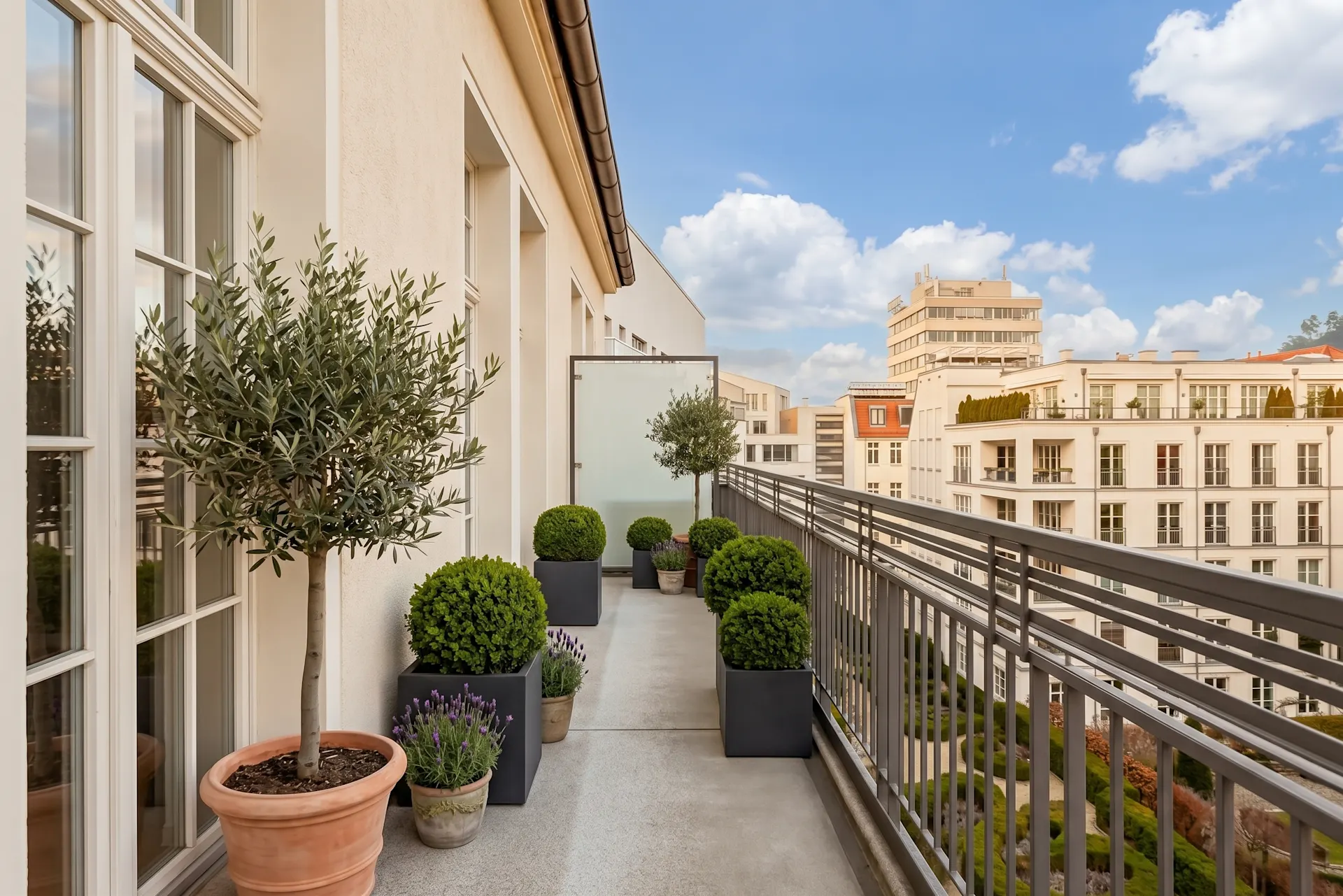 Langer Balkon mit zahlreichen Pflanzen in Töpfen und Blick auf benachbarte Wohngebäude.