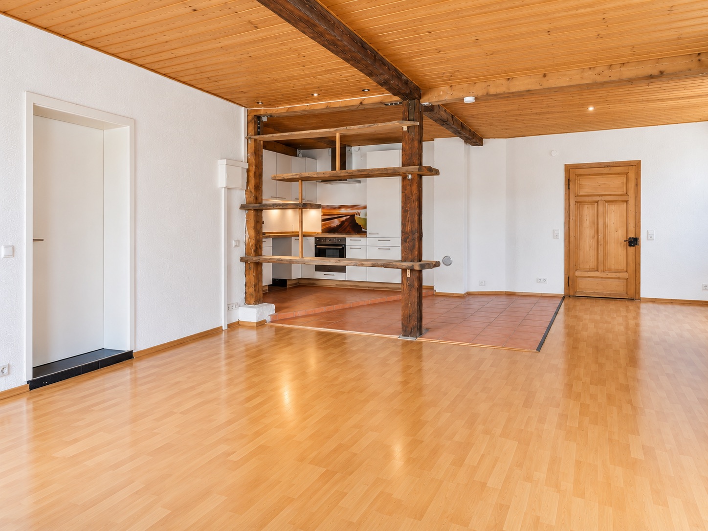 Heller Wohnraum mit Holzboden, offener Küche und Holzbalken an Decke und Raumteiler.