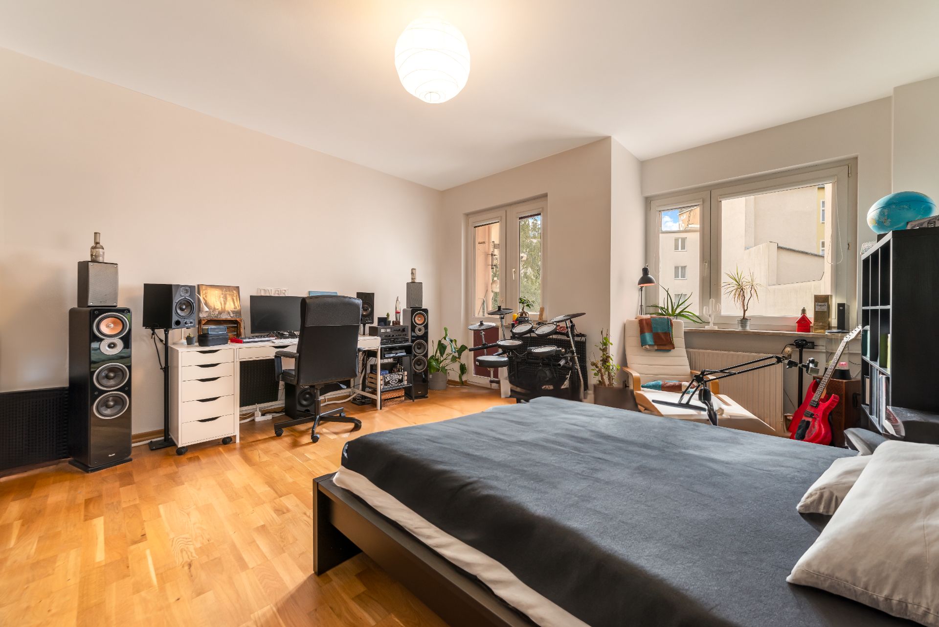Helles Schlafzimmer mit Schreibtisch, Musikinstrumenten, Bett und großen Fenstern.