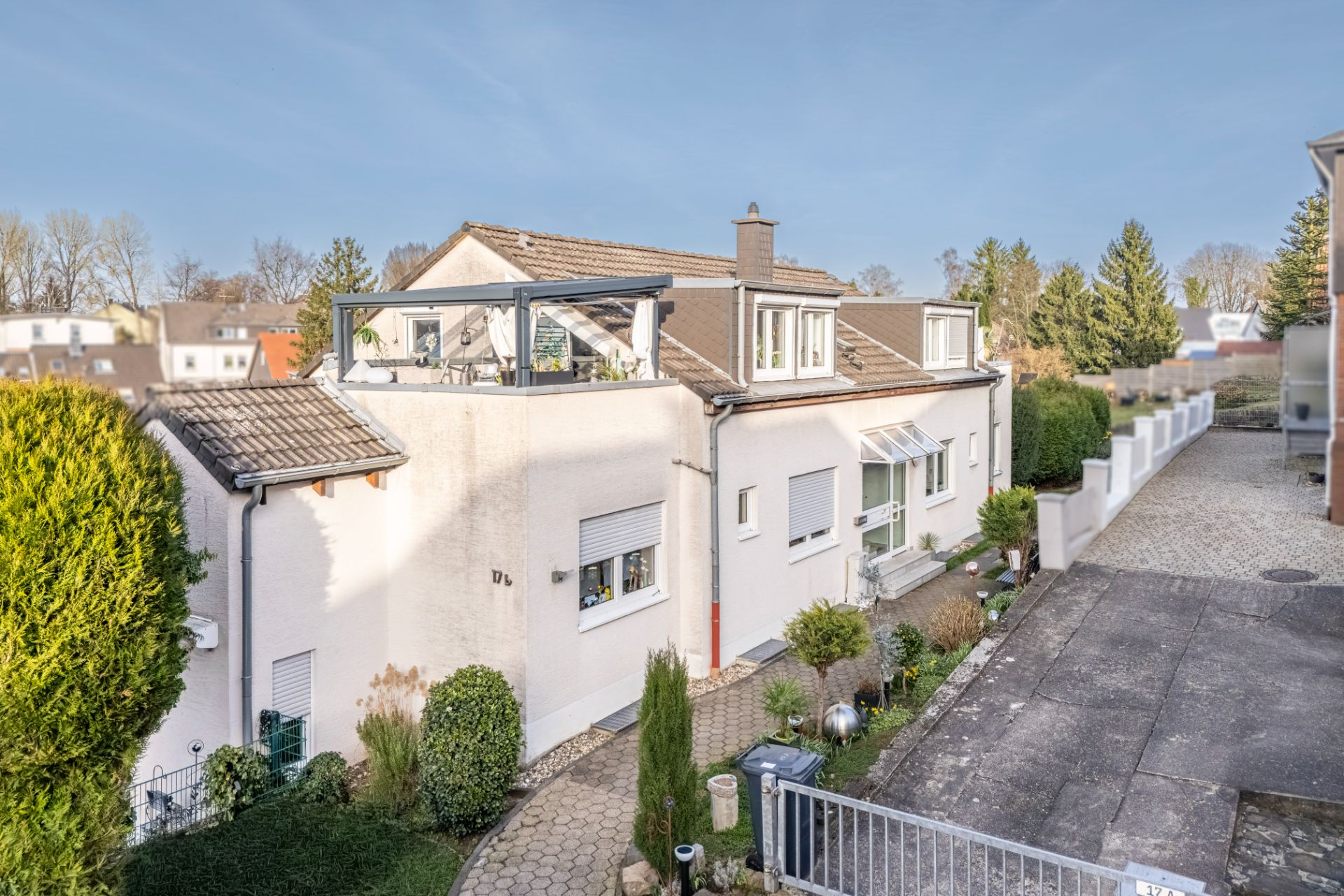 Modernes, weißes Einfamilienhaus mit Terrasse und Garten, neben einer Einfahrt, bei sonnigem Wetter.