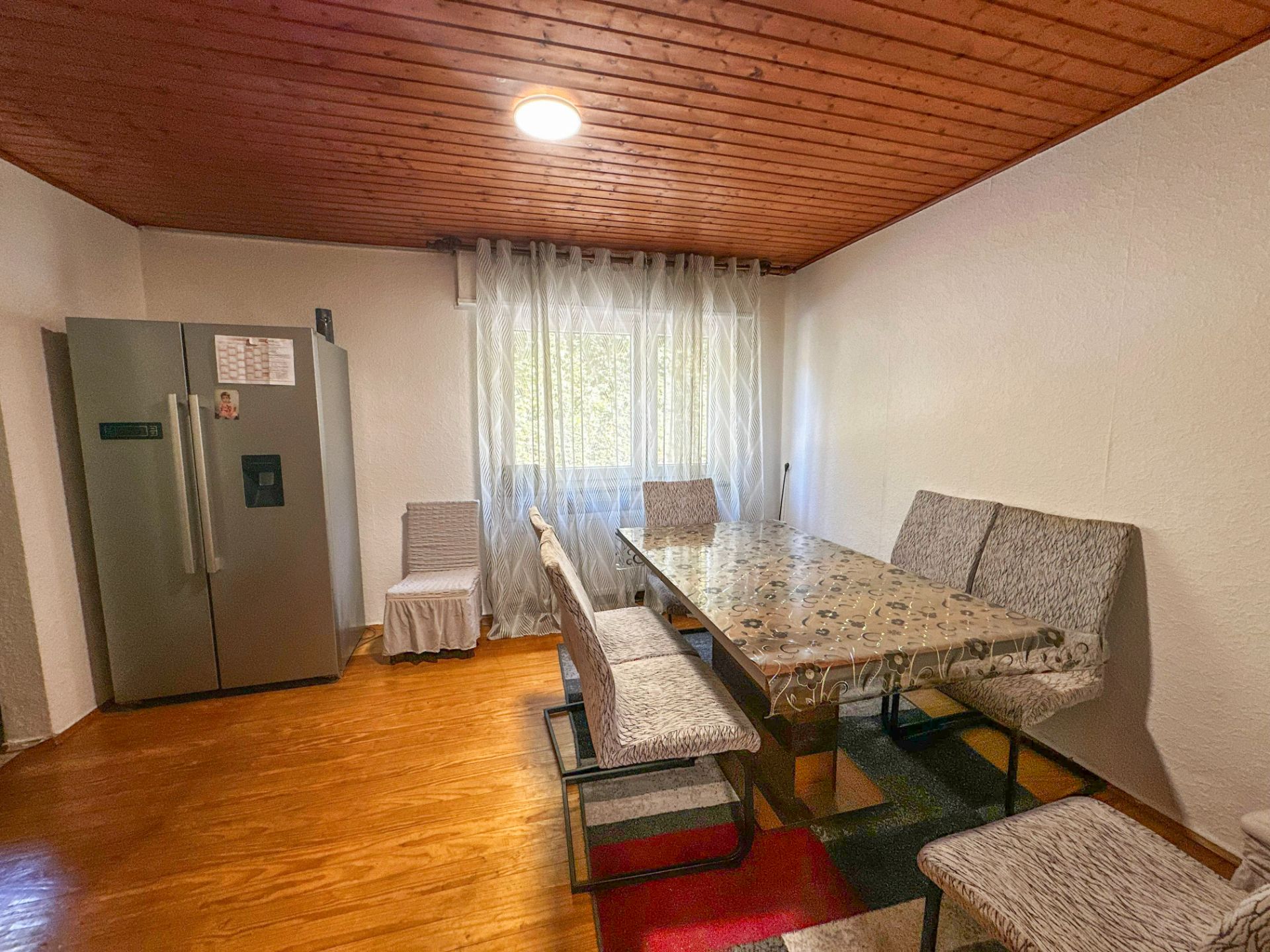 Essbereich mit großem Tisch, sechs gepolsterten Stühlen und einem Kühlschrank auf Holzfußboden.