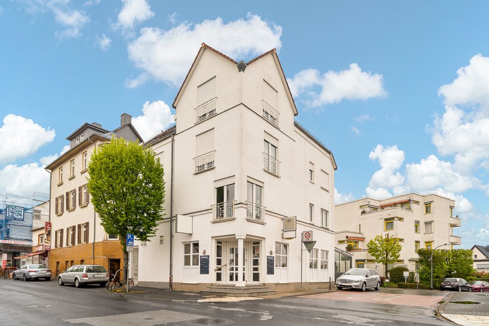 Weiße Wohngebäude an einer Straßenecke mit geparkten Autos und Bäumen.