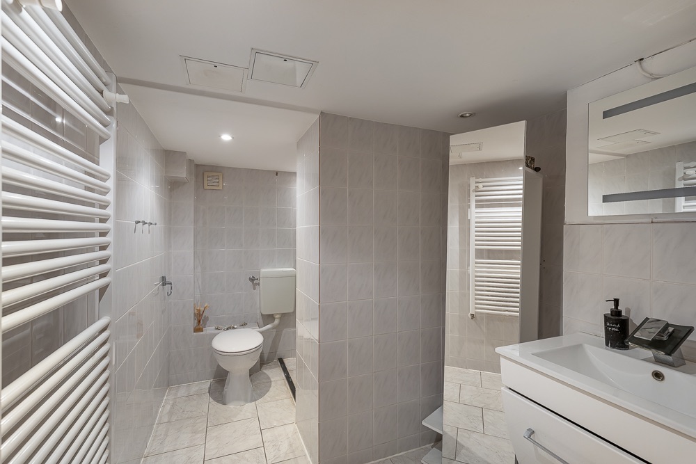 Modernes Badezimmer mit Toilette, Dusche, Waschbecken und Handtuchheizkörper.