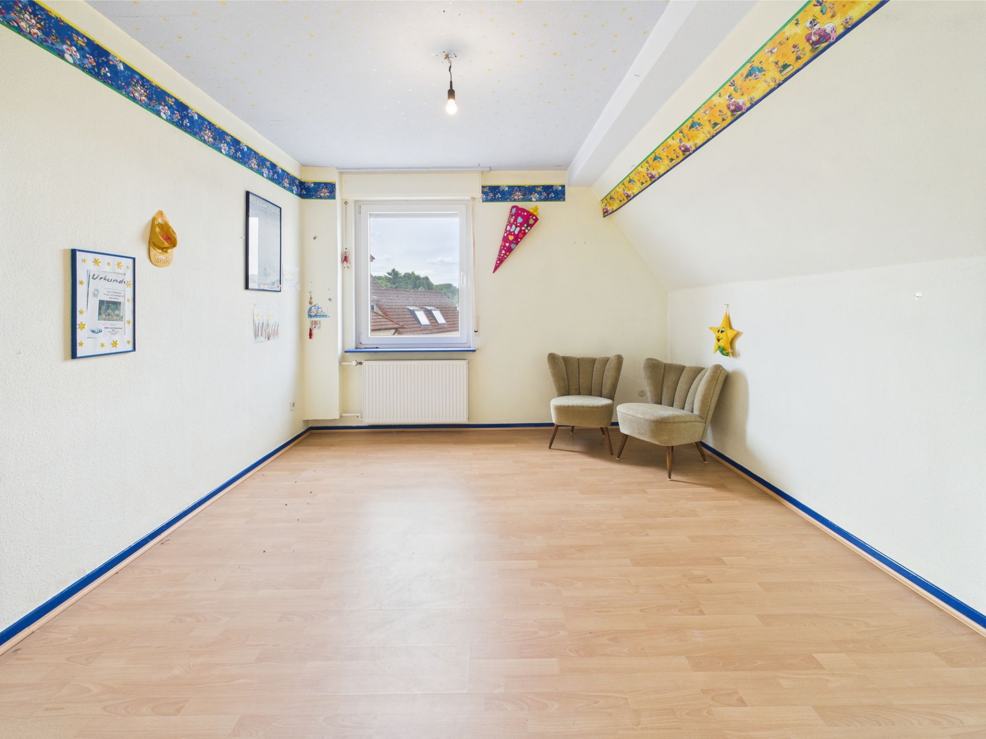 Helles Kinderzimmer mit Holzfußboden, zwei Sesseln und einem Fenster mit Blick nach draußen.