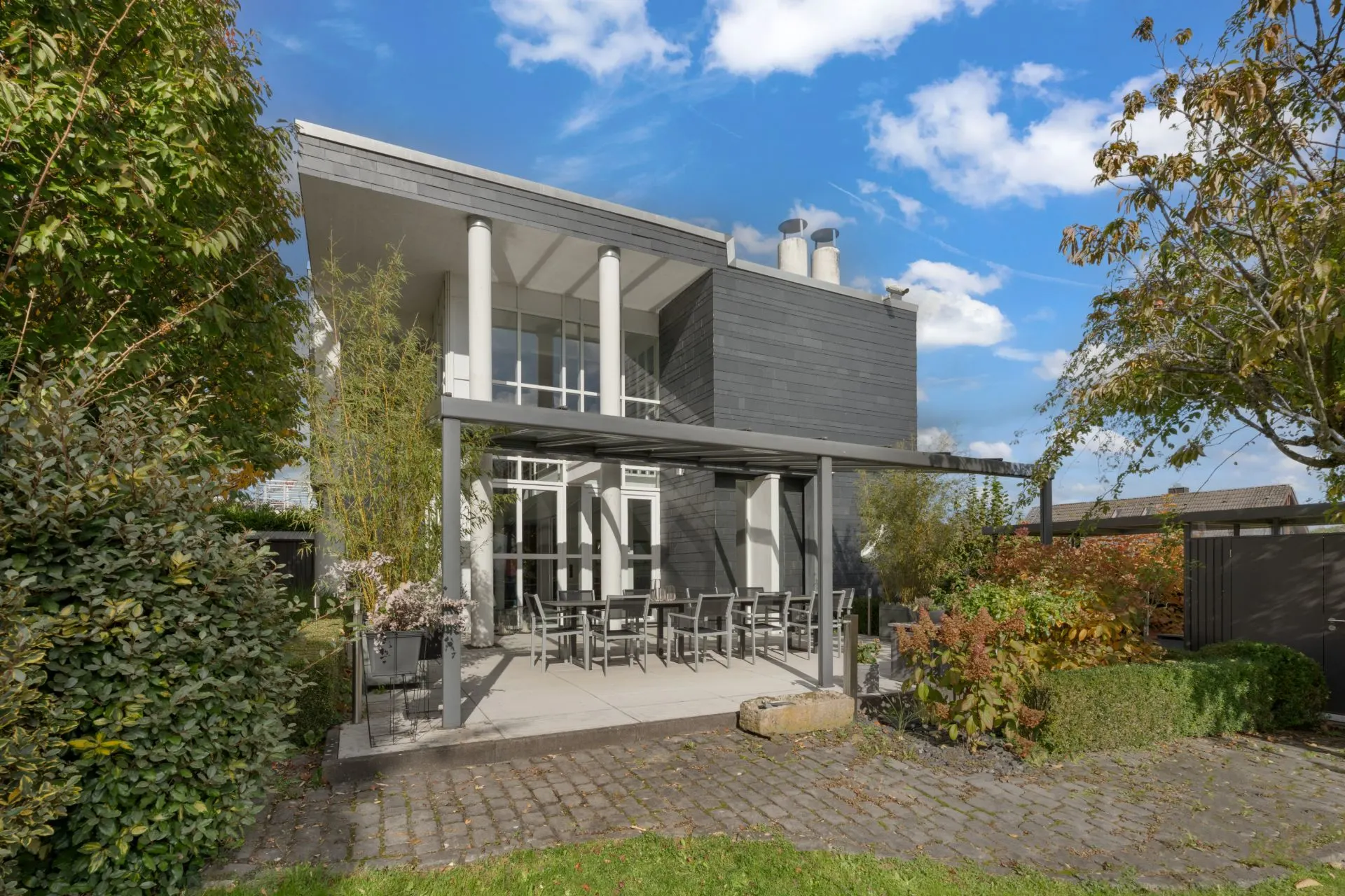Modernes Wohnhaus mit großer Terrasse, Gartenmöbeln und umliegendem Garten im Freien.