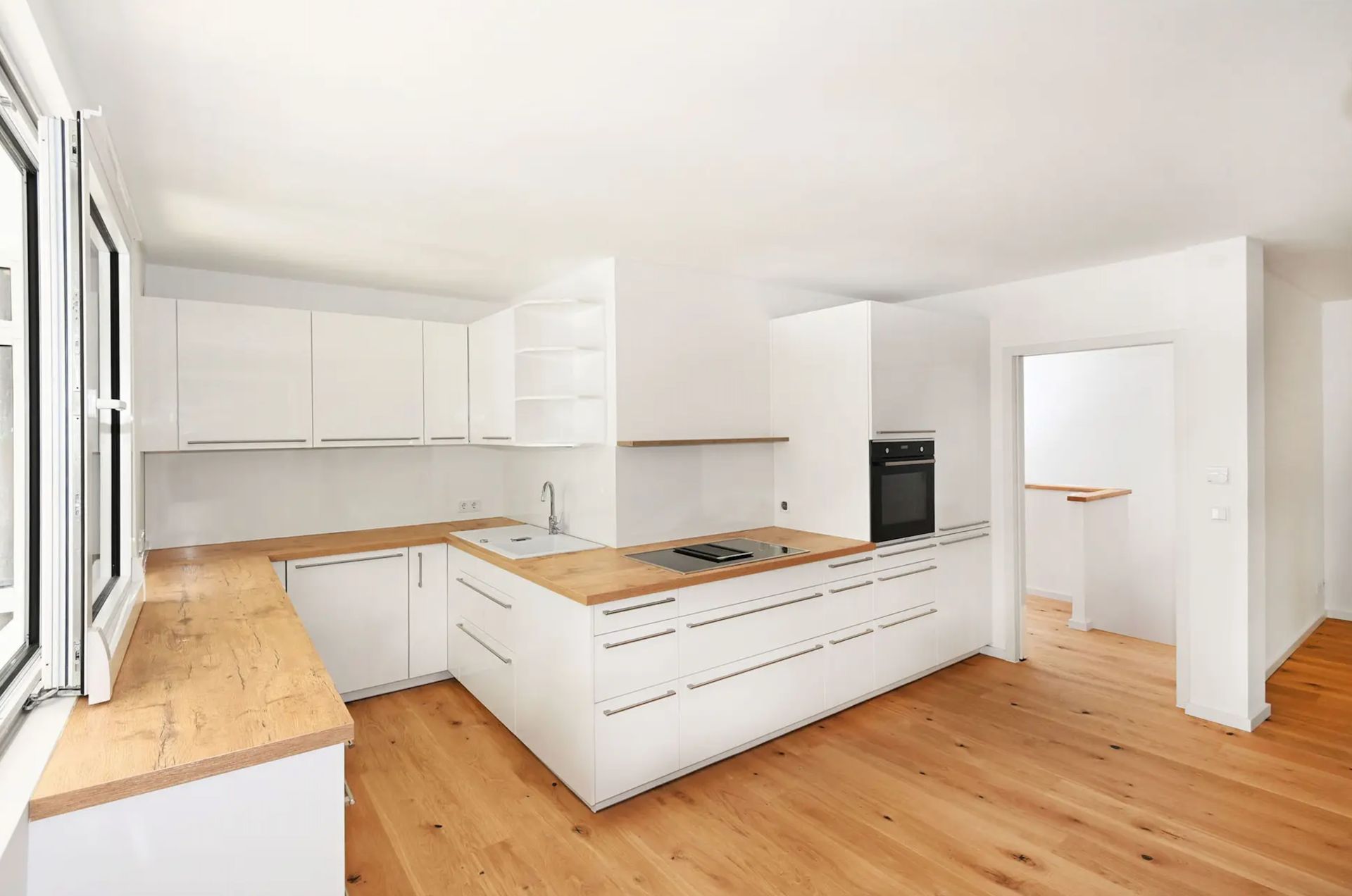 Moderne, helle Küche mit weißen Schränken, Holzarbeitsplatten und offenem Fenster.