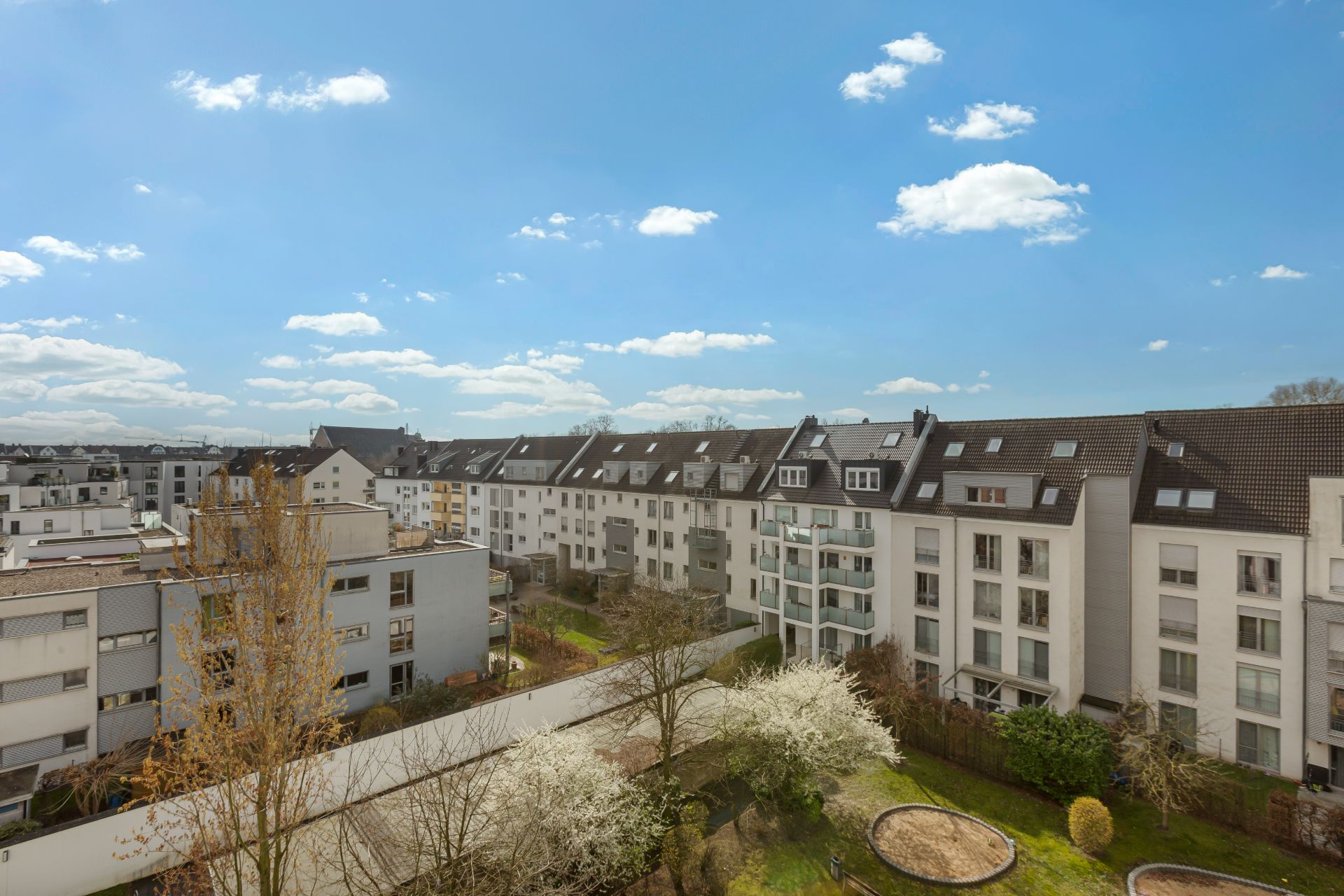 Blick auf mehrere Wohngebäude mit Gärten und Bäumen unter blauem Himmel.