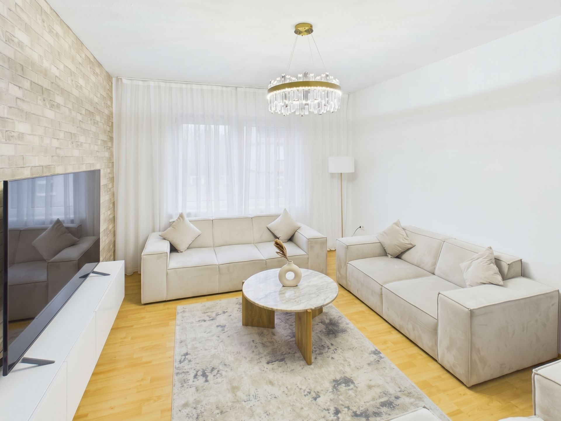 Modernes Wohnzimmer mit zwei hellen Sofas, Couchtisch, Teppich, Fernseher und Kronleuchter.
