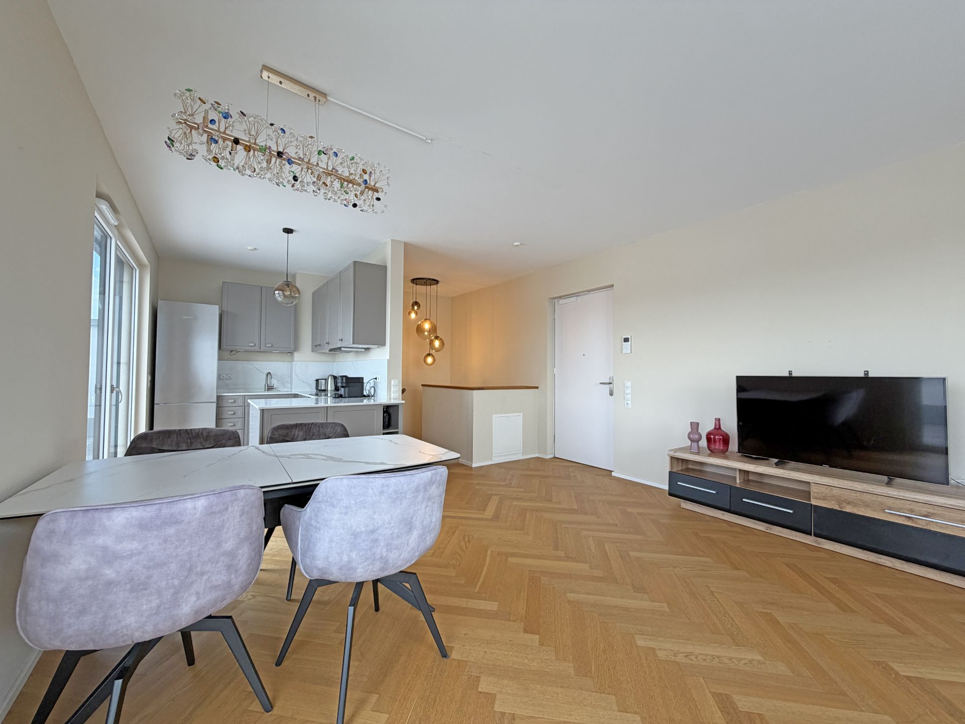 Offener Wohnraum mit Esstisch, Küche und Fernseher auf Holzfußboden.